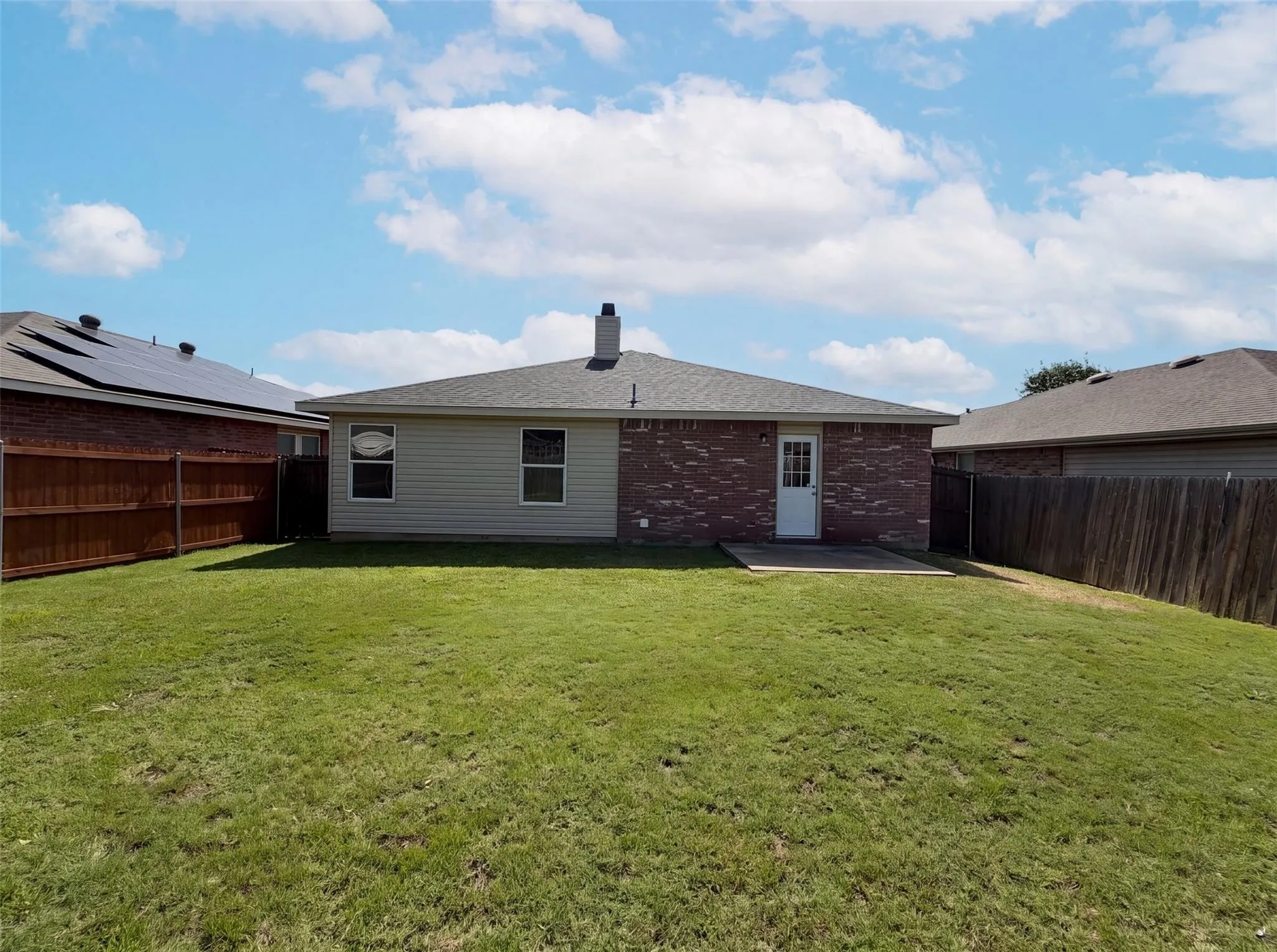 Expansive grassy backyard featuring a private wood fence, a concrete patio, and a brick and siding exterior