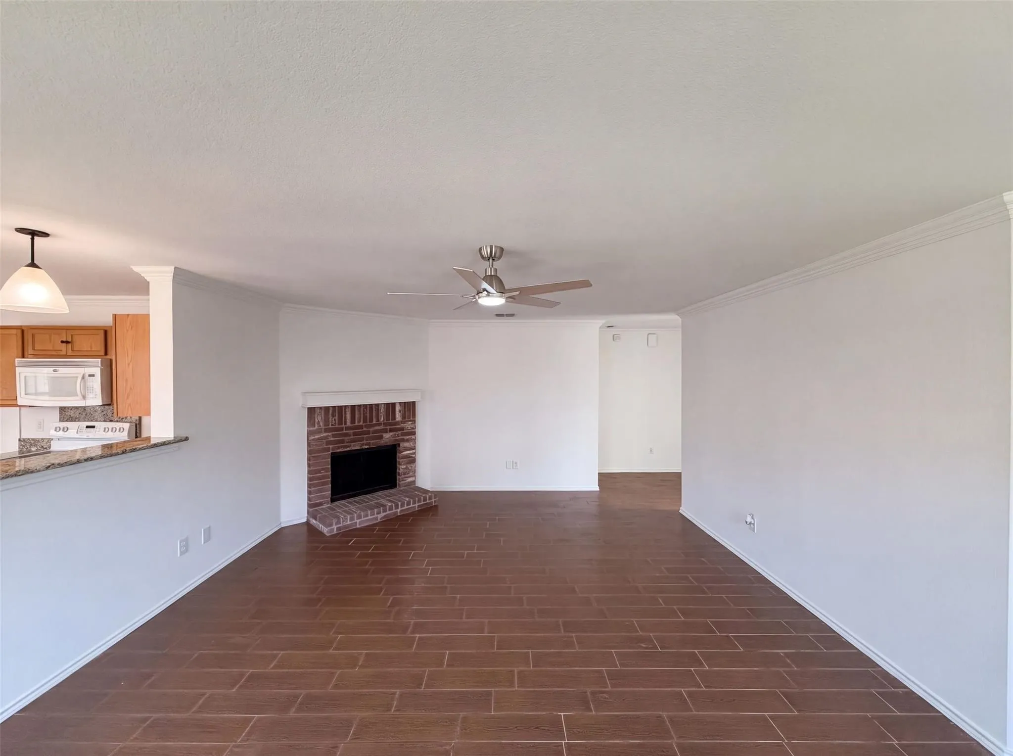 Brick fireplace with hearth, wood-finish flooring, ceiling fan, crown molding, and recessed wall space