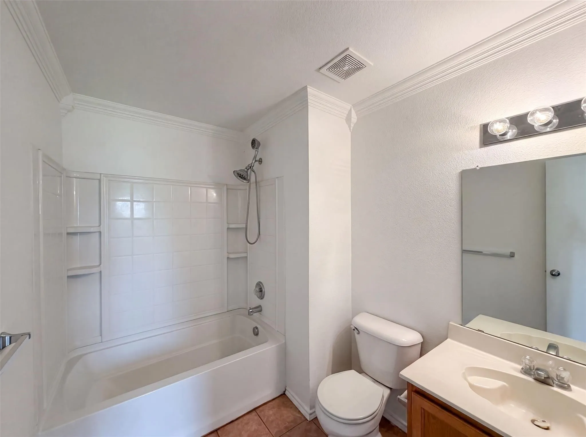 Bathroom featuring a tub/shower combination with tiled surround, a wood-finish vanity with an integrated sink, a wall-mounted mirror, and crown molding