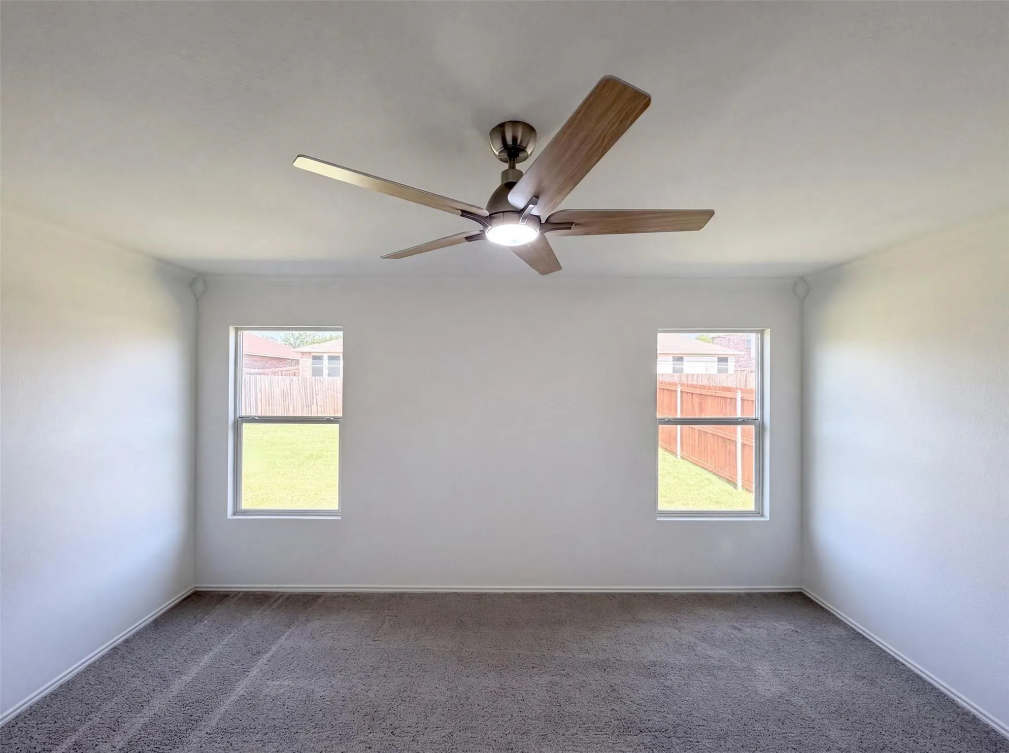 Neutral wall paint, ceiling fan with wood-finish blades and integrated lighting, carpet flooring, and two vertical windows