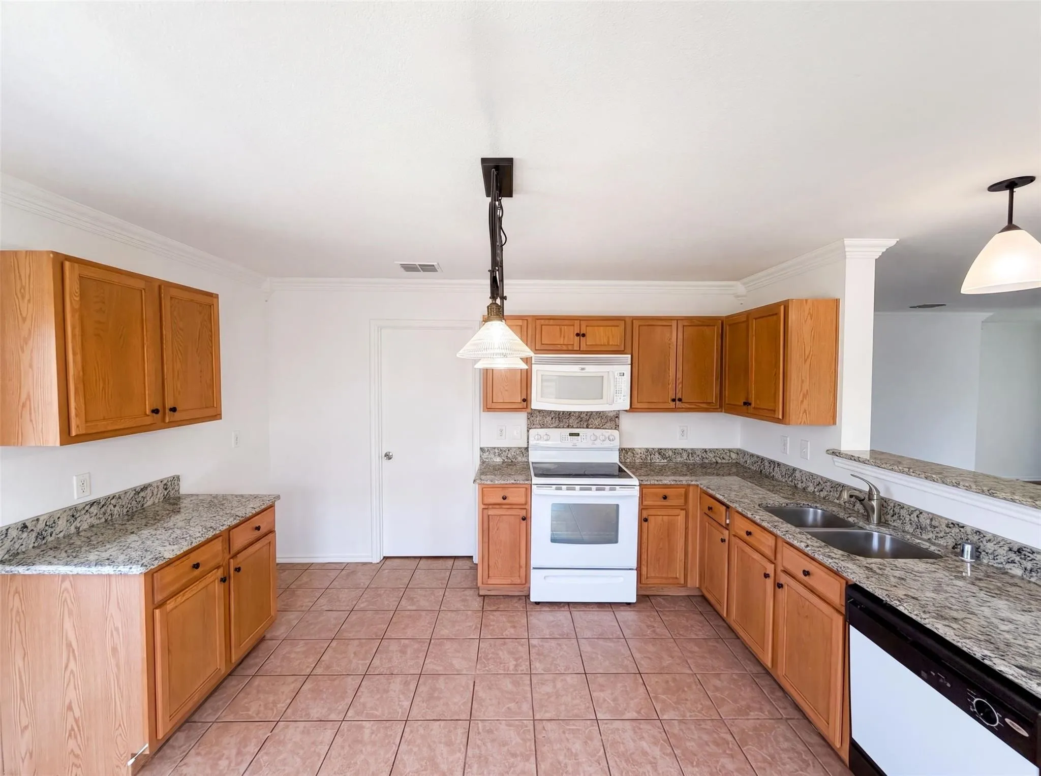 Spacious kitchen featuring wood cabinetry, stone countertops, a double-basin sink, and tile flooring