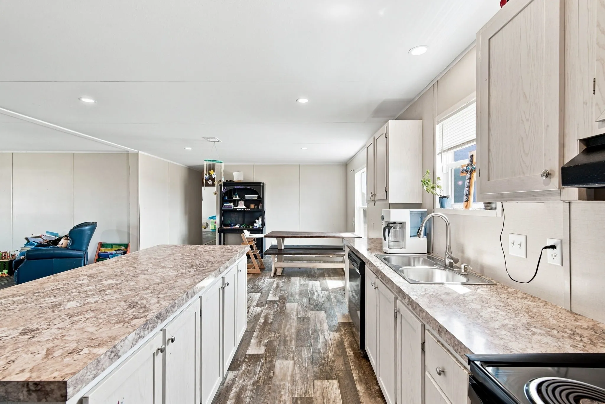 Kitchen featuring light-toned cabinetry, a spacious island with a stone-finish countertop, wood-finish flooring, recessed lighting, and a stainless steel sink