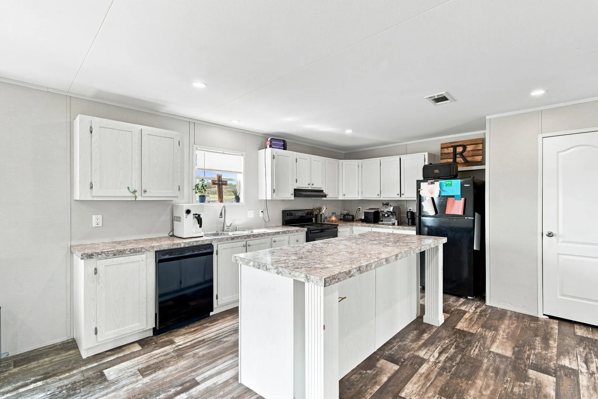 Bright kitchen featuring white cabinetry, a central island with a stone-finish countertop, wood-finish flooring, a built-in dishwasher, and recessed lighting