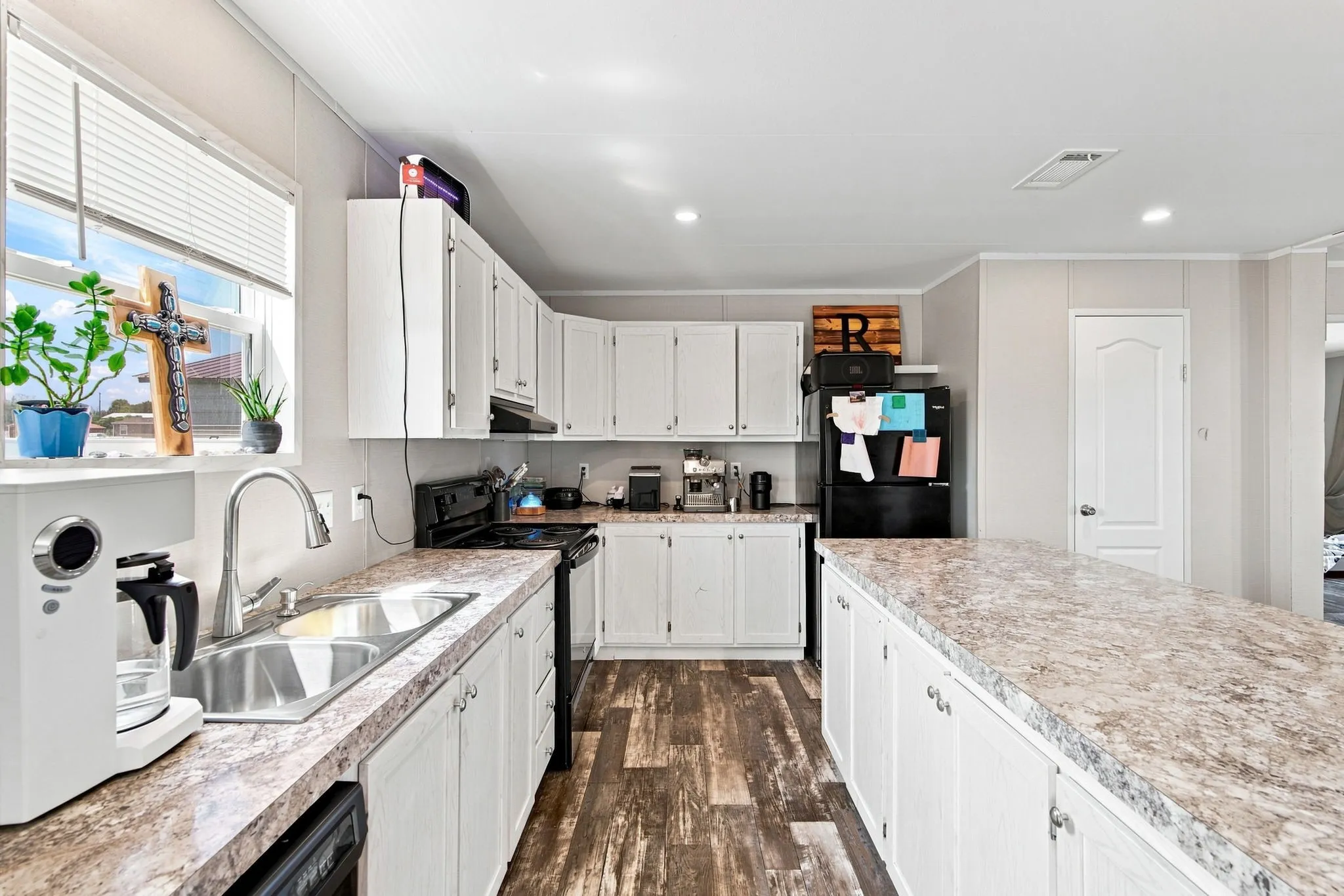 Kitchen featuring white cabinetry, a large kitchen island, wood-finish flooring, a double basin sink, and a black appliance package