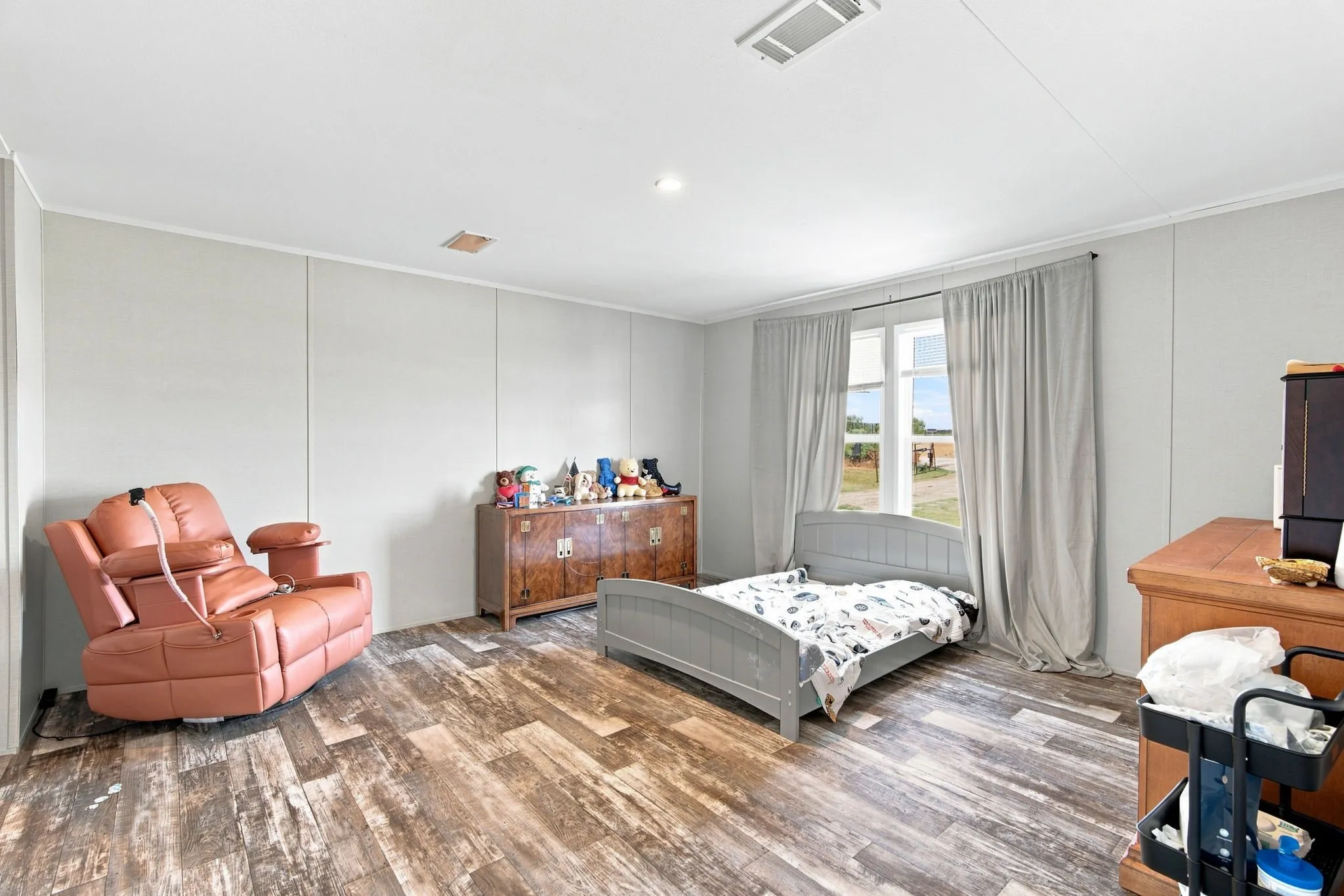 Spacious room featuring wood-finish flooring, light grey panel walls, and a large window with ample natural light