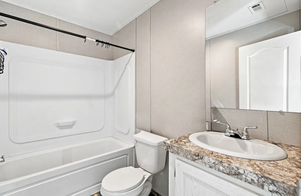 White bathtub with a shower unit, commode, wall-mounted mirror, and vanity with a built-in sink