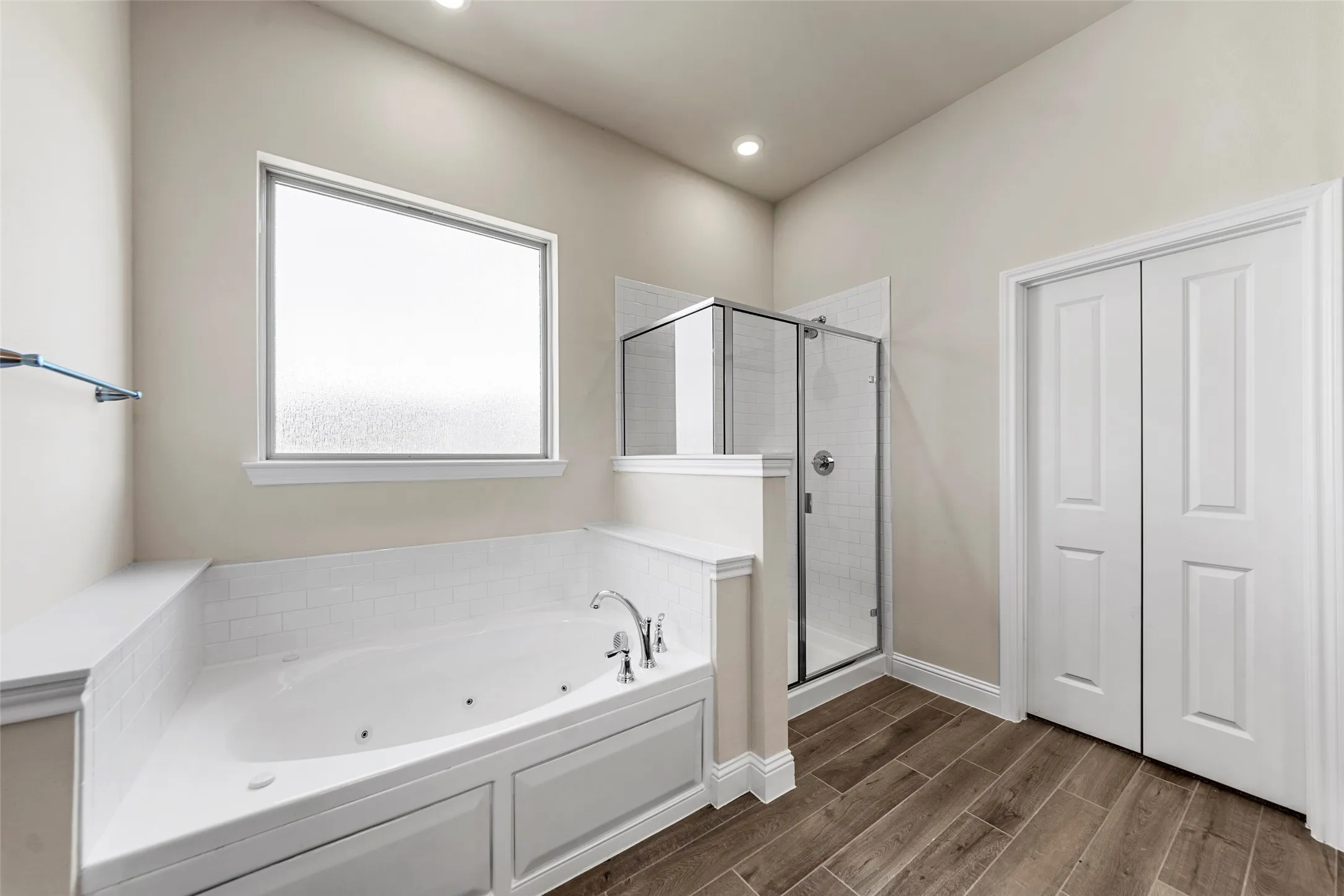 Soaking tub with a white subway tile surround, separate glass-enclosed shower, wood-look flooring, and recessed lighting