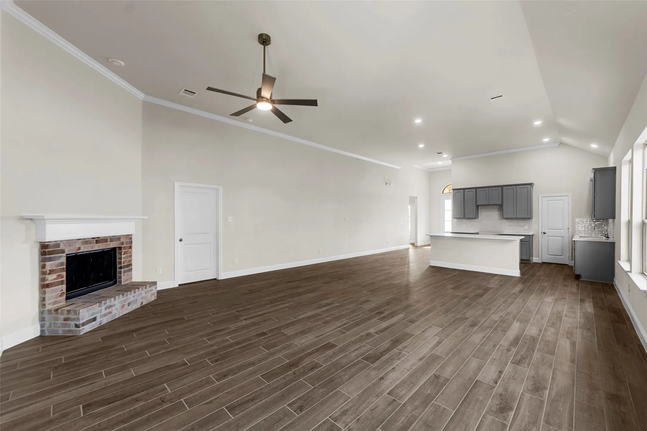 Spacious living area with wood-finish flooring, a brick fireplace, and vaulted ceilings