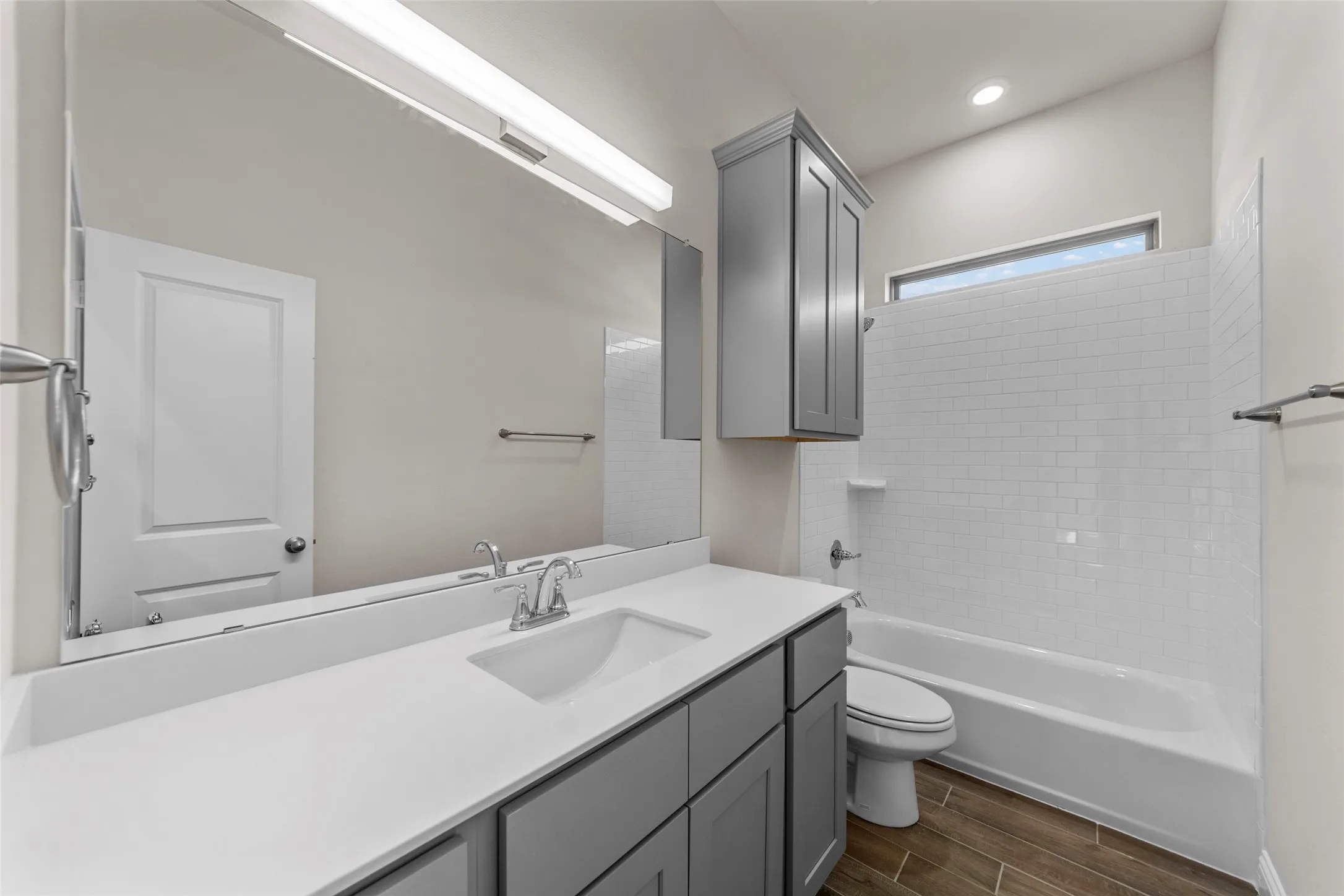 Dual sink vanity with a light countertop, wood-finish flooring, white subway tile shower surround, and a high window