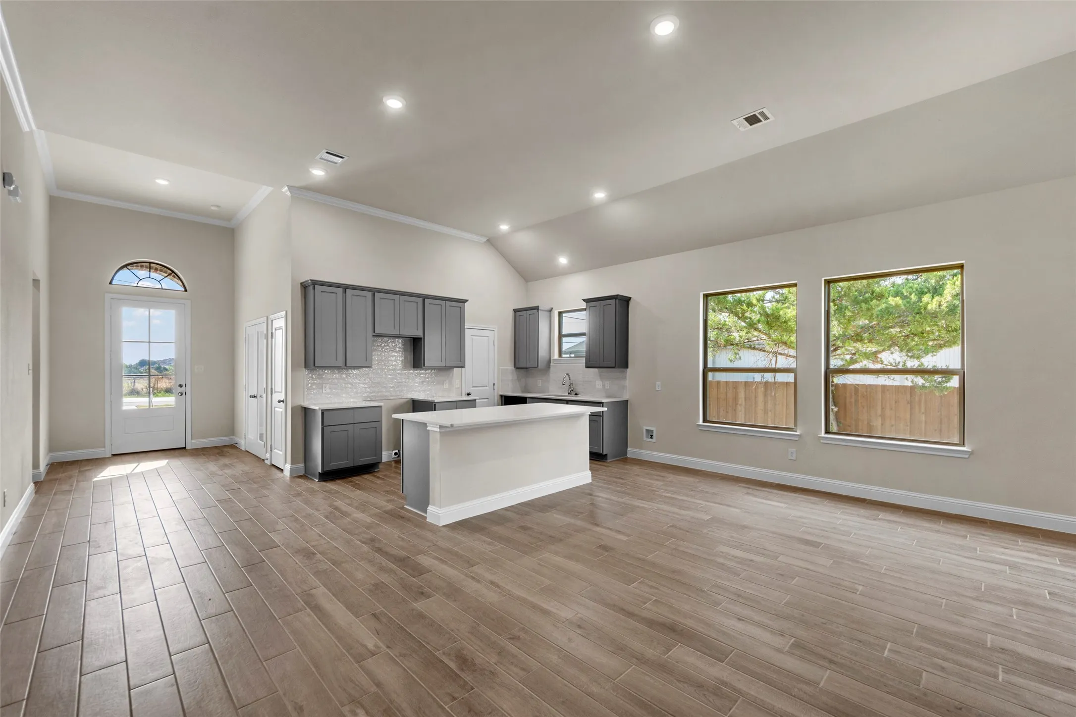 Vaulted ceilings, wood-finish flooring, gray cabinetry, white subway tile backsplash, and an arched transom window above the entry