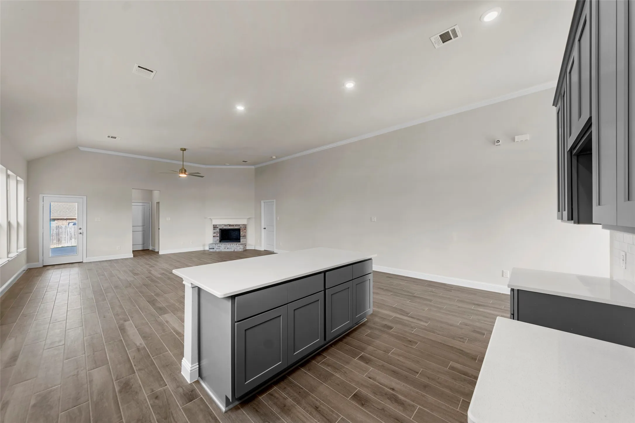 Spacious common area featuring vaulted ceilings, wood-finish flooring, a kitchen island with stone countertops, recessed lighting, and a fireplace with a stone surround