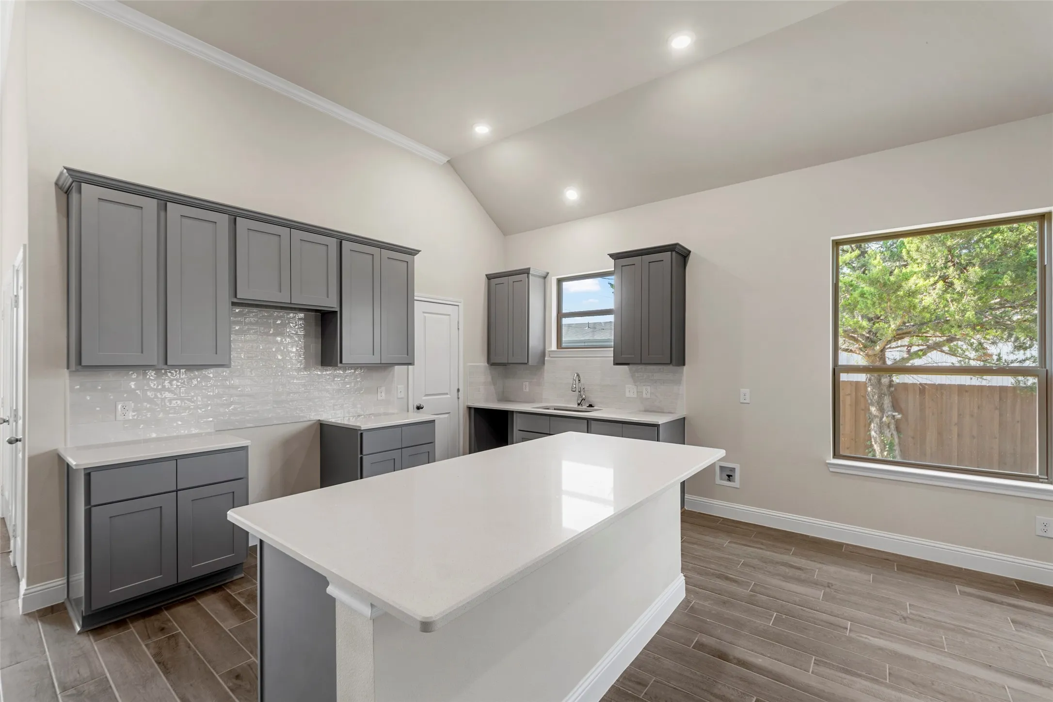 Vaulted ceiling, recessed lighting, wood-finish flooring, white countertop surfaces, and gray cabinetry