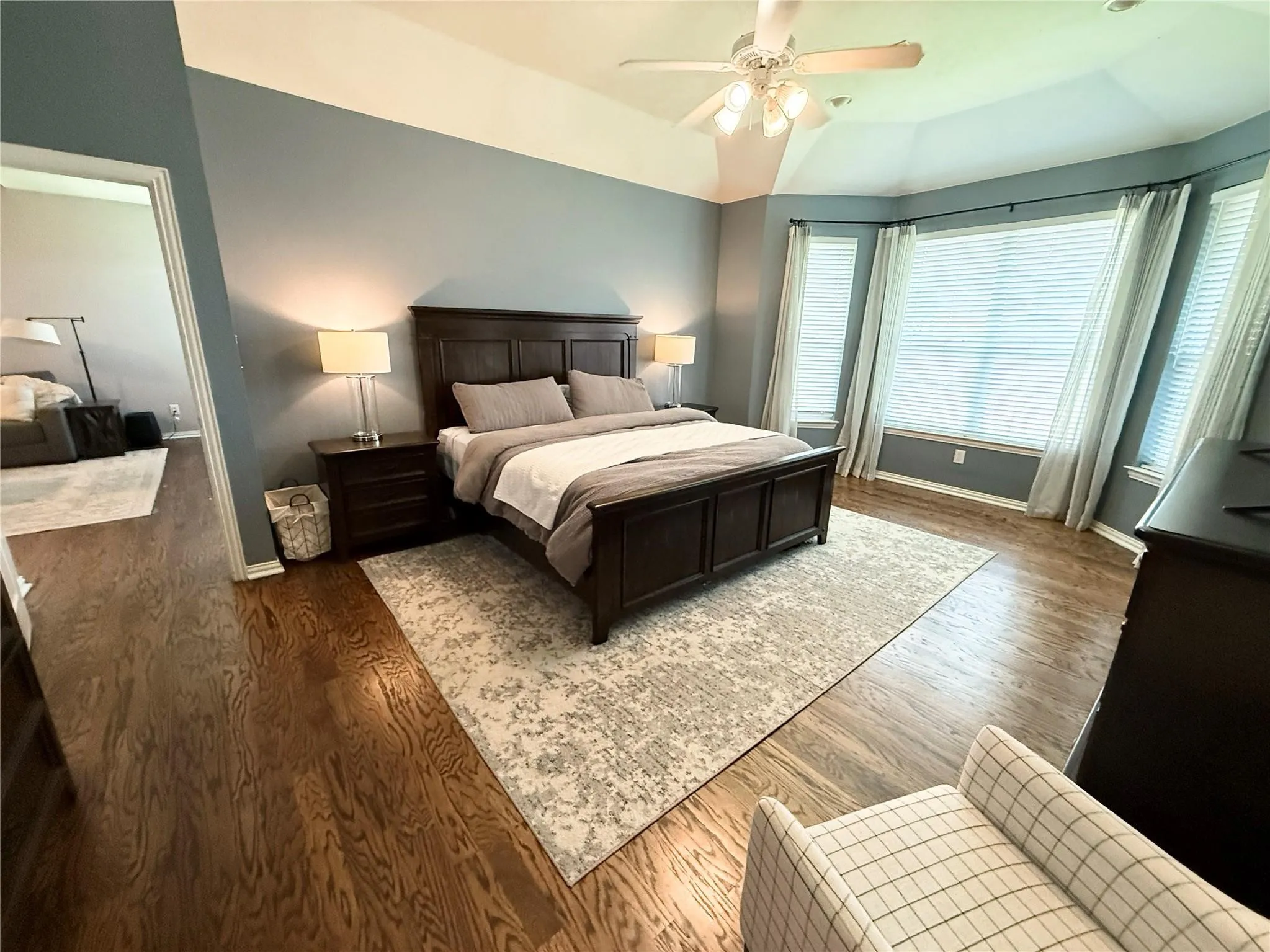 Wood-finish flooring throughout, tray ceiling, ceiling fan with light fixture, bay window with multiple panes, and interior doorway