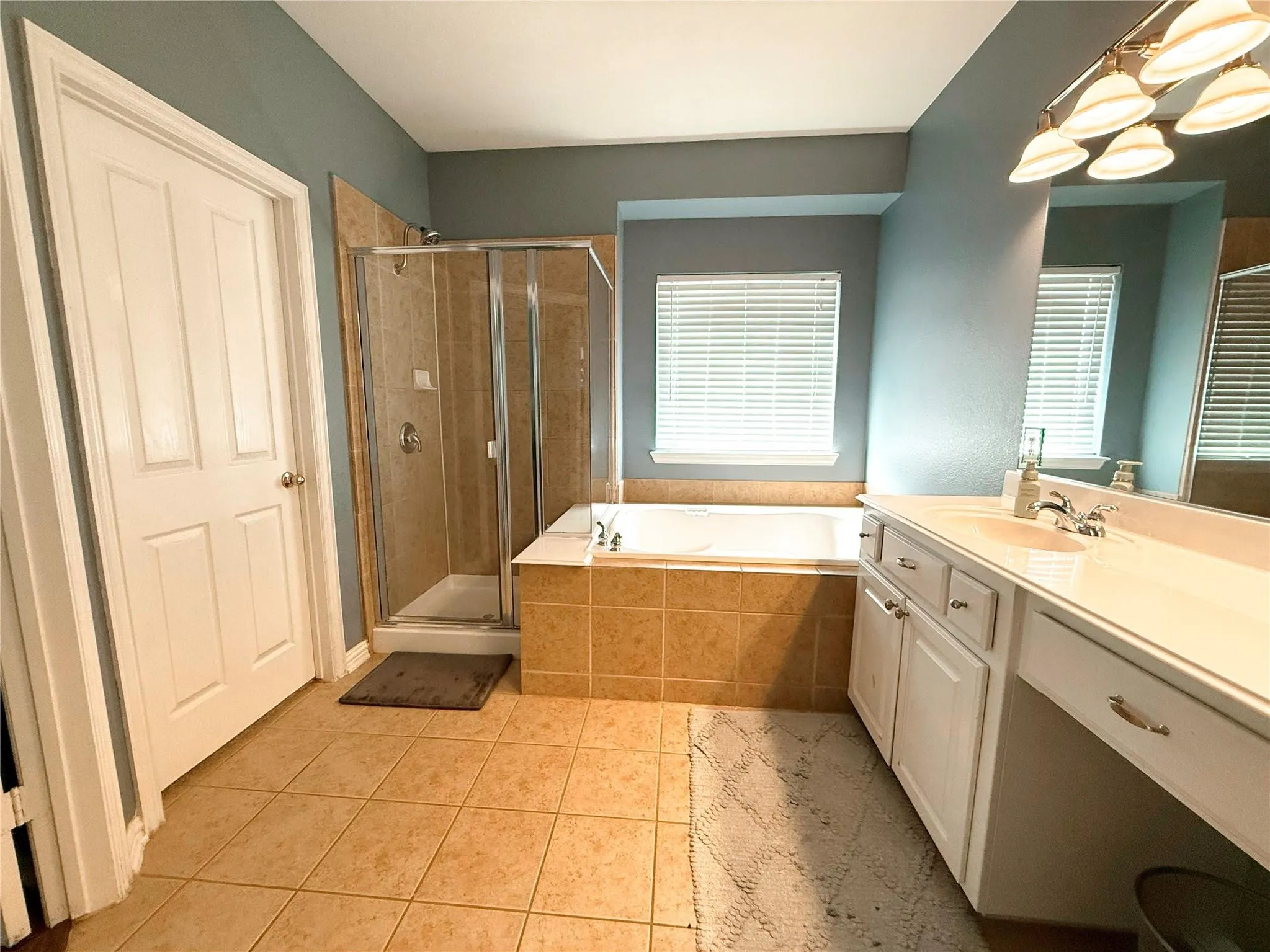 Tiled flooring, white paneled door, built-in soaking tub, glass-enclosed shower, and a vanity with integrated sink