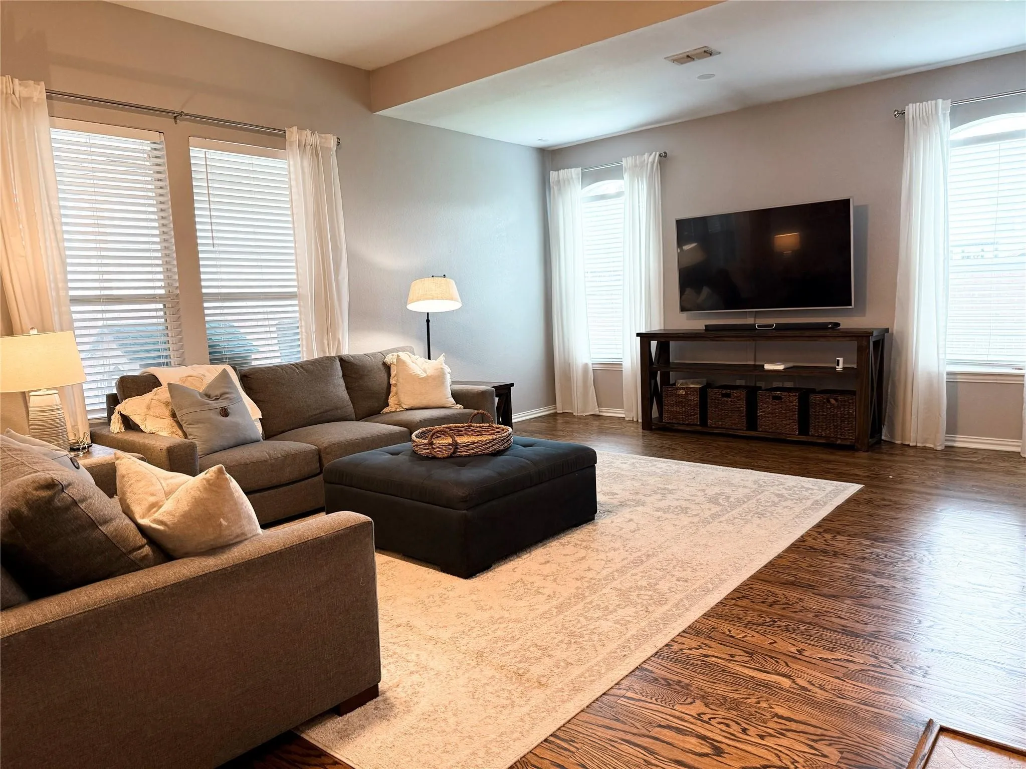 Spacious living area featuring a dark wood entertainment console with open shelving, recessed ceiling lighting, and hard wood-finish flooring throughout