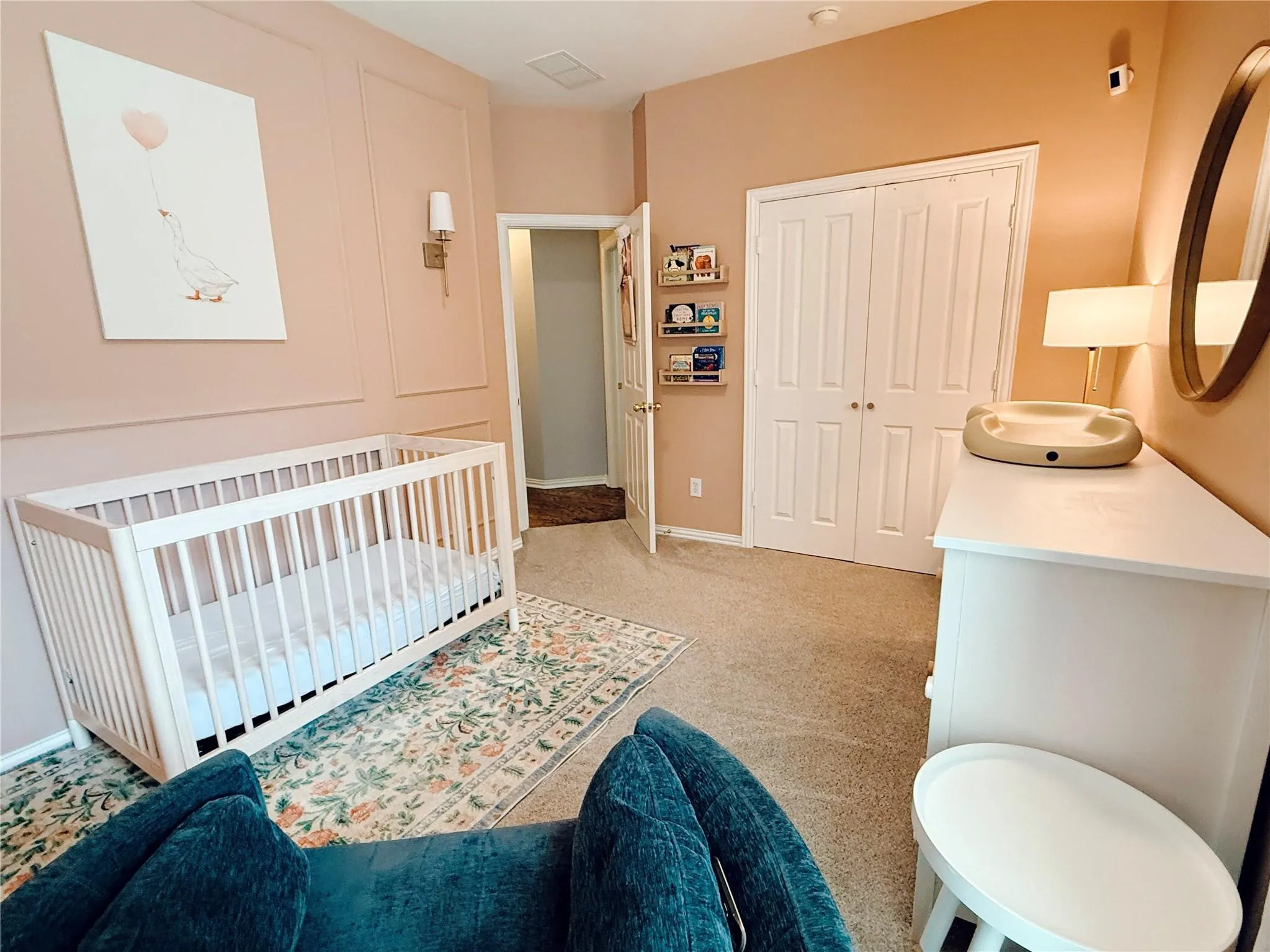 Serene nursery featuring soft peachy-orange walls, white six-panel closet doors, and neutral carpet flooring