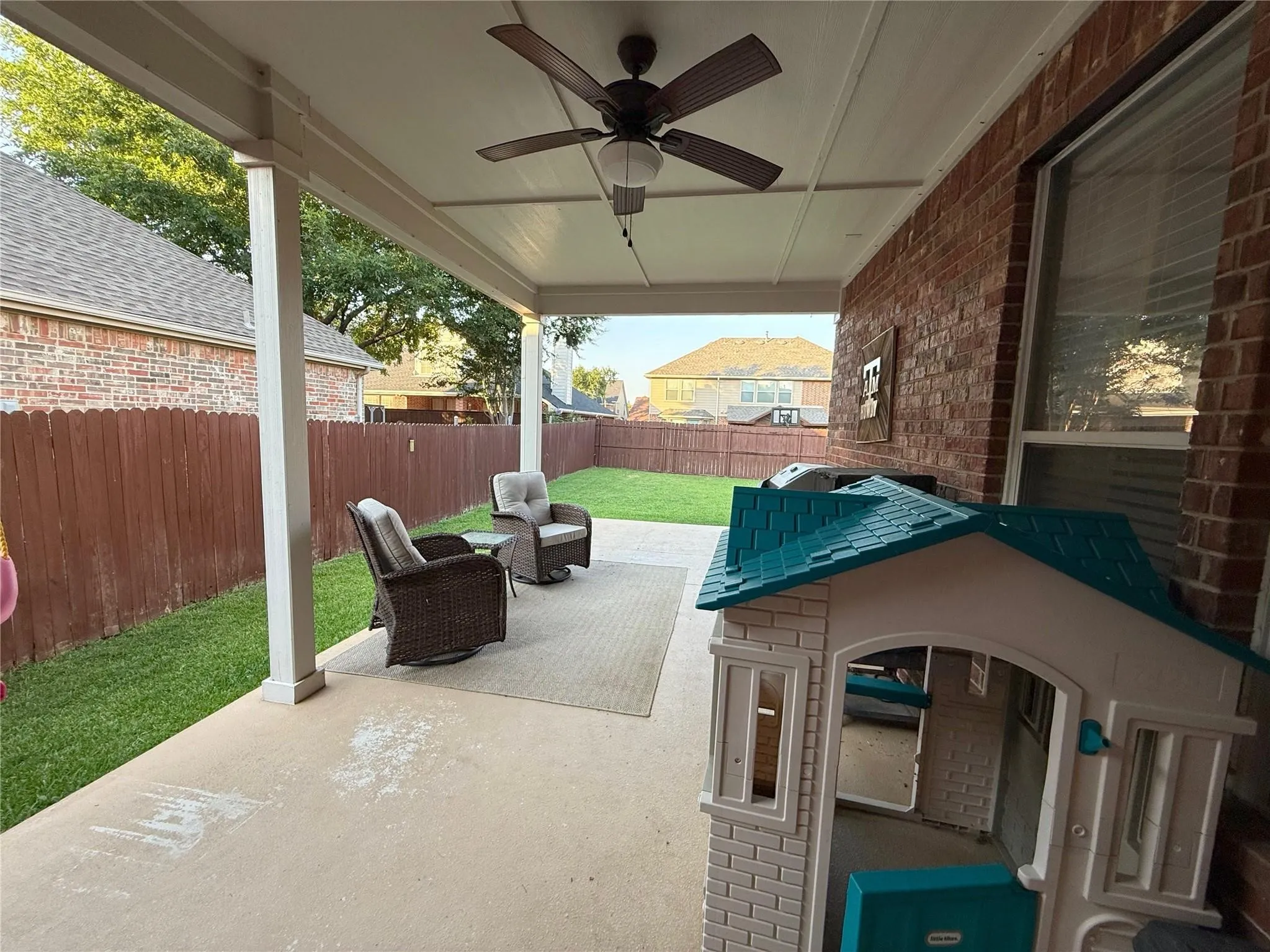Covered patio with a ceiling fan, concrete flooring, brick exterior, and a fenced yard with manicured lawn
