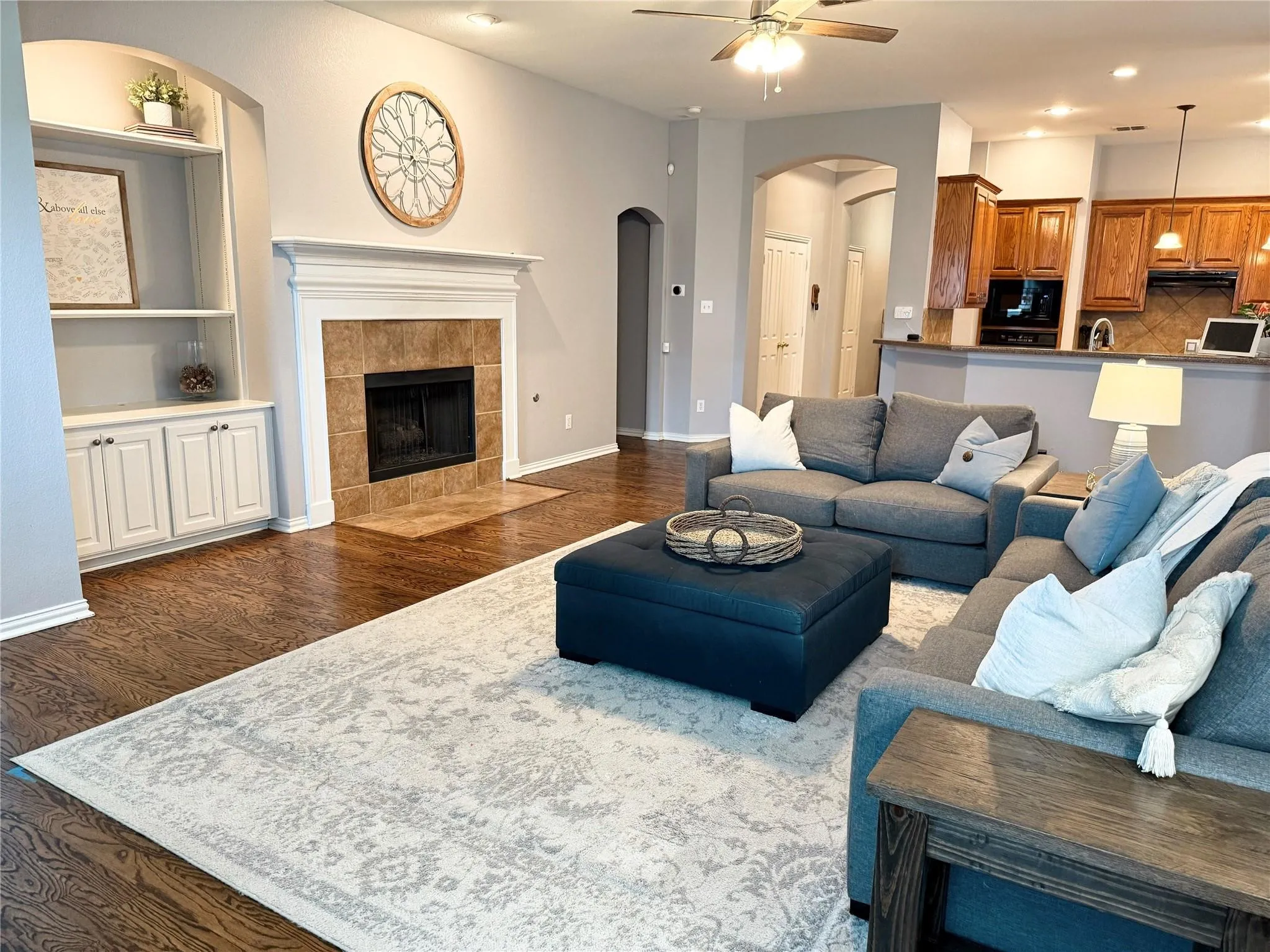 Living area featuring wood-finish flooring, a fireplace with a tile surround and mantel, built-in cabinetry with shelving, and recessed lighting