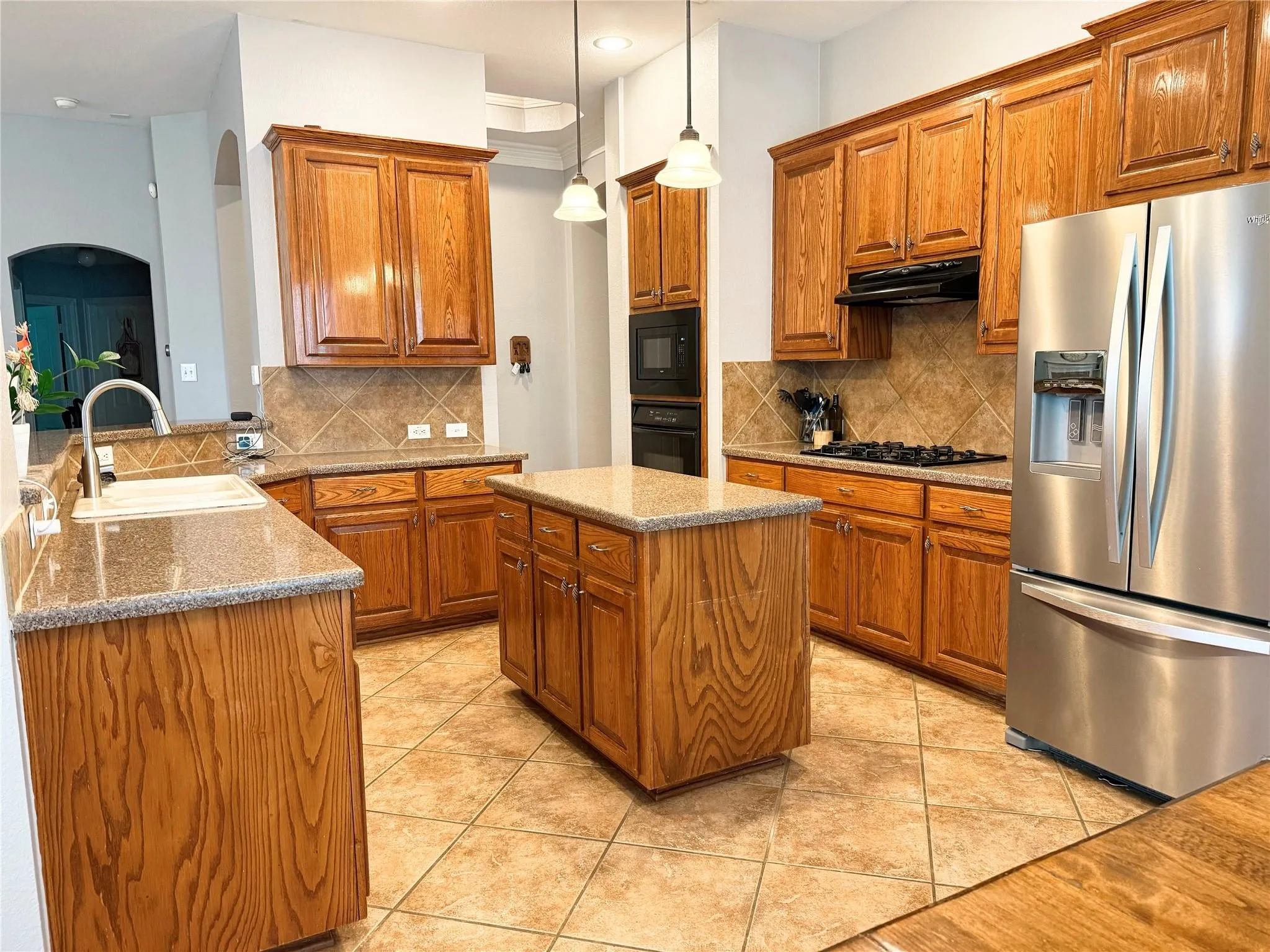 Kitchen with wood cabinetry, granite-finish countertops, stainless steel appliances, and tile flooring