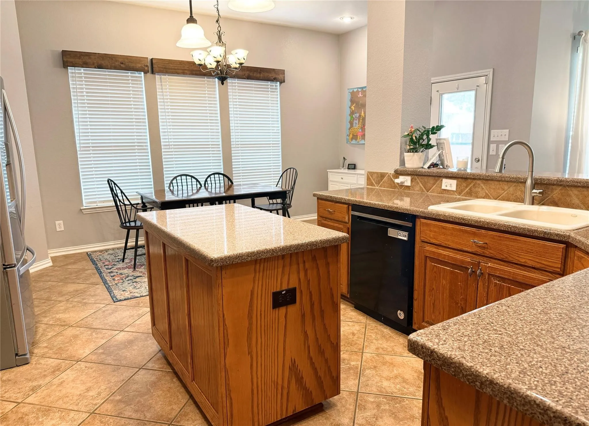 Kitchen featuring an island, light wood-finish cabinetry, speckled countertops, and a double basin sink