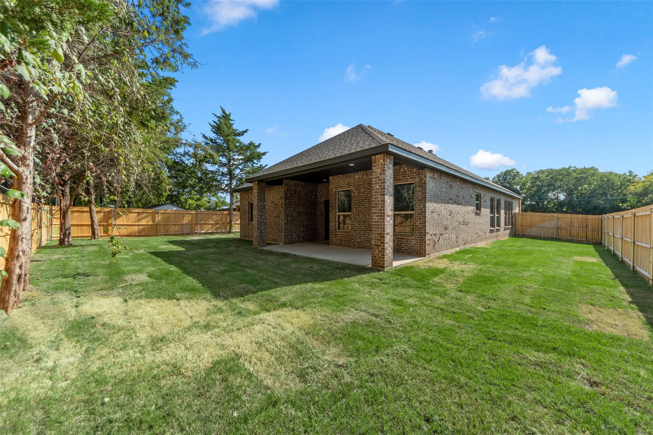 Brick exterior with a covered patio, expansive lawn, and wood privacy fencing