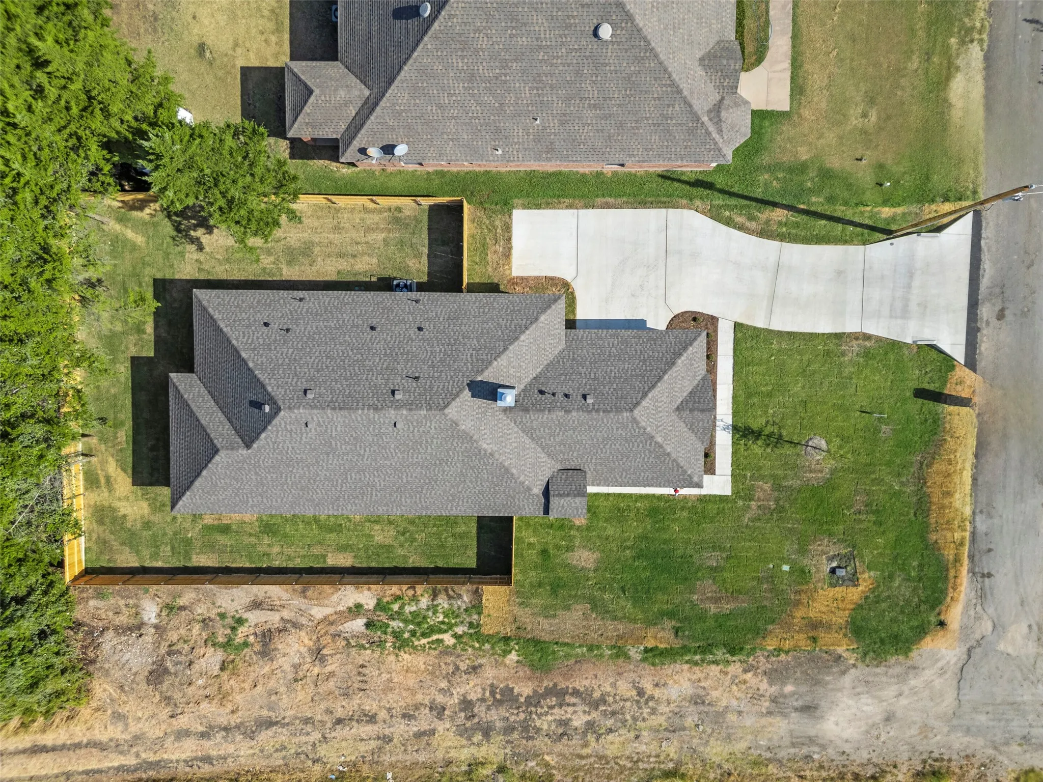 Residential property featuring a gray shingle roof, concrete driveway, and a partially fenced backyard