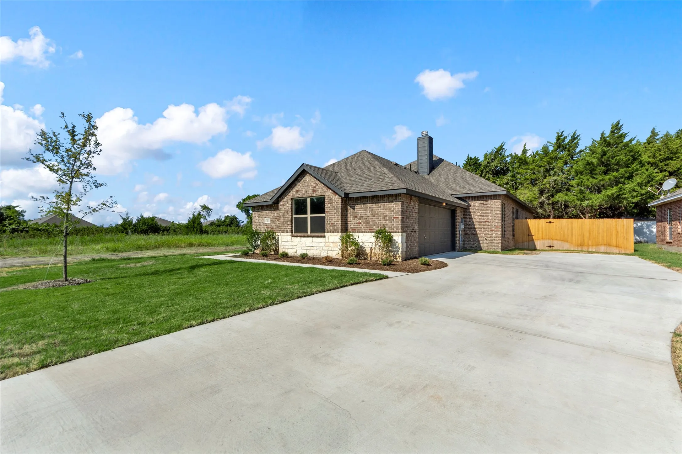 Brick and stone-veneer exterior with a two-car garage, concrete driveway, front lawn, and wood privacy fence