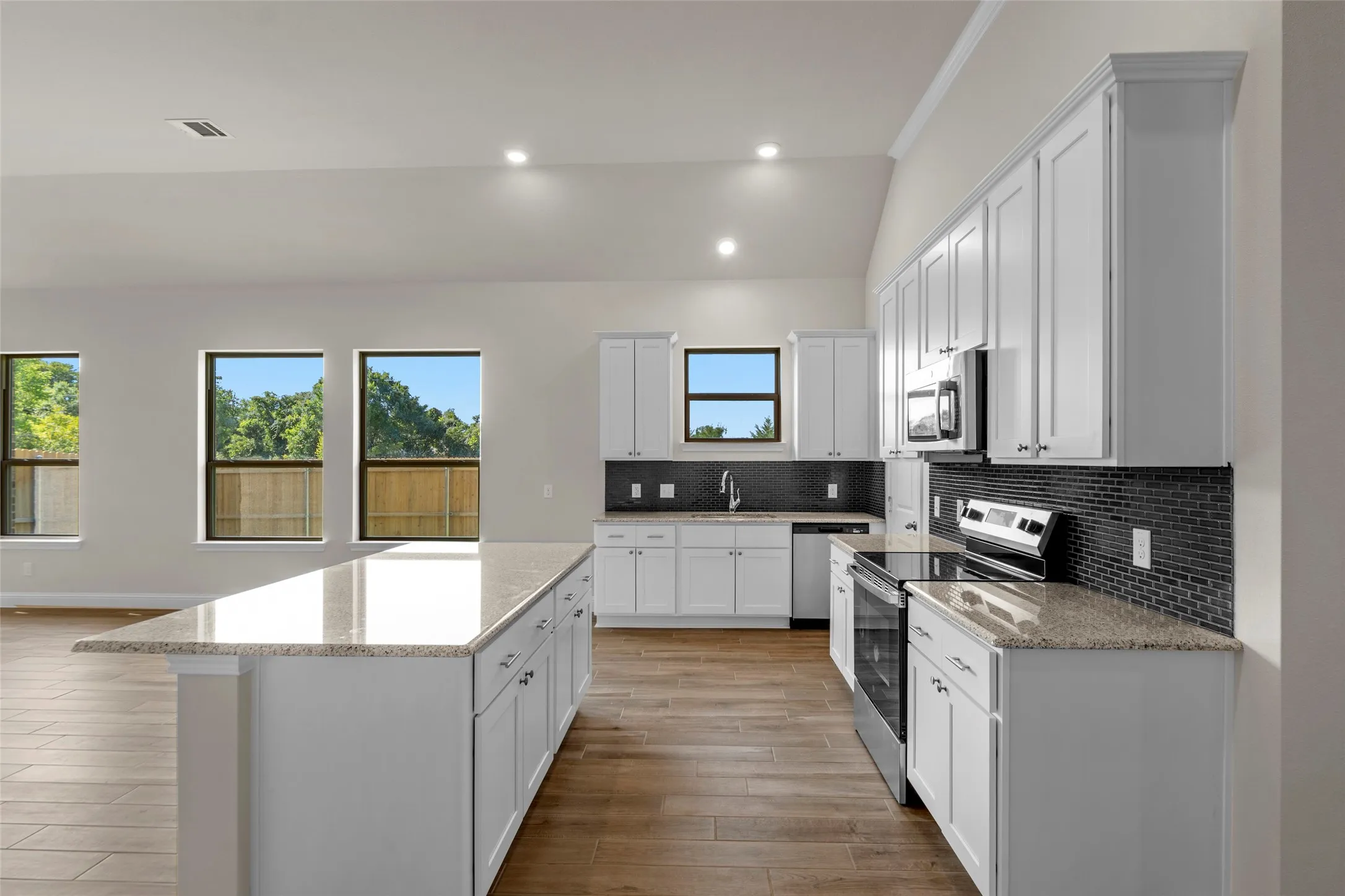 Kitchen featuring white cabinetry, light-toned countertops, stainless steel appliances, and a dark tile backsplash