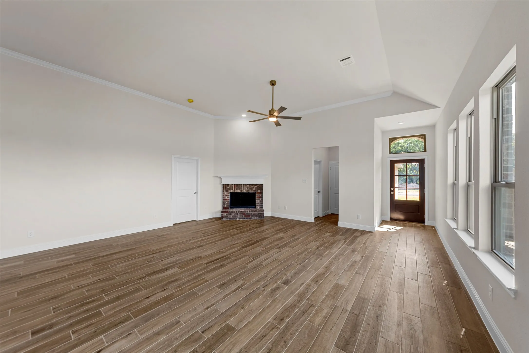 Spacious living area featuring wood-finish flooring, a vaulted ceiling, and a brick fireplace