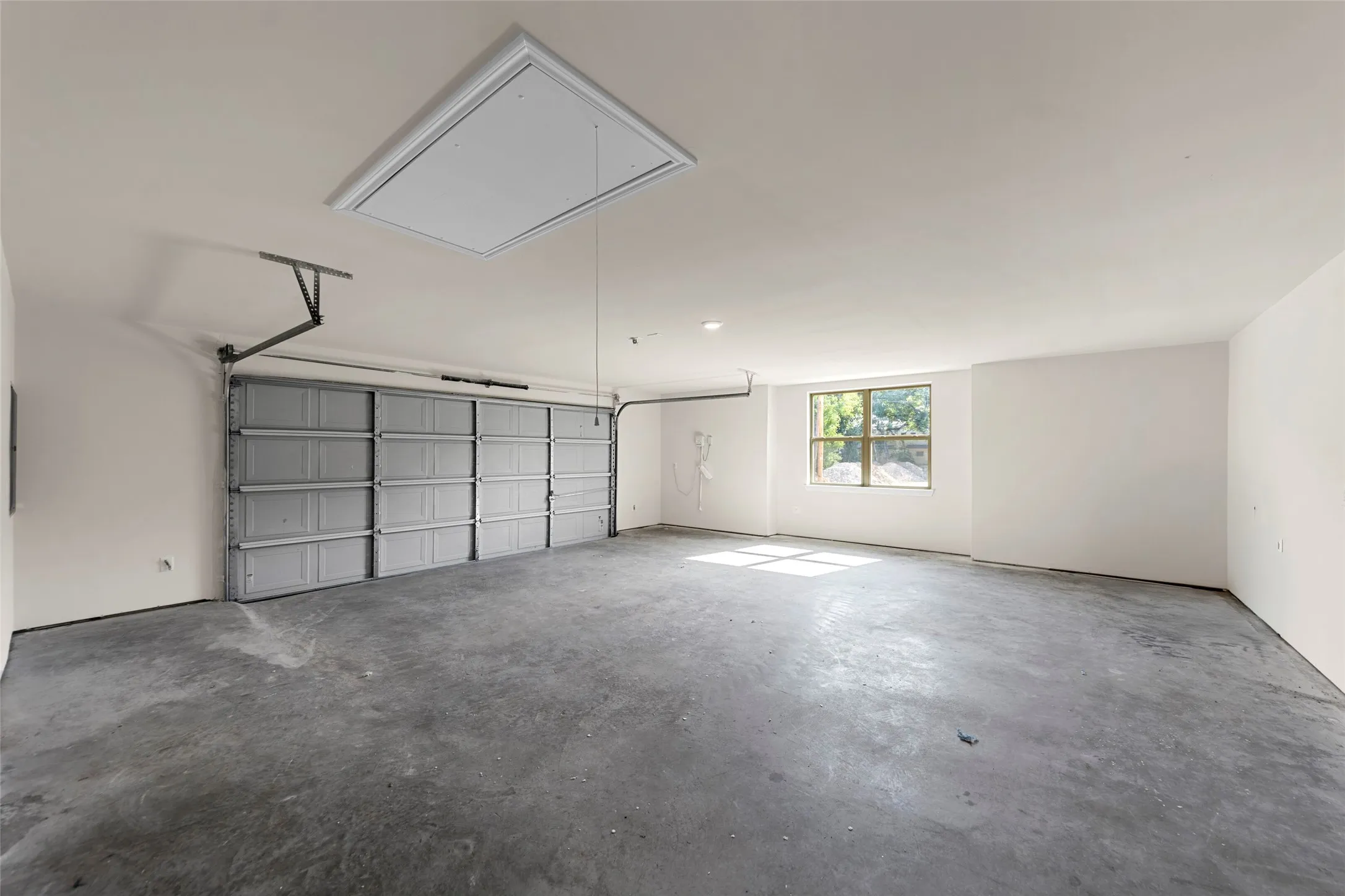 Spacious garage with concrete flooring, a large overhead door, an access panel, and a window