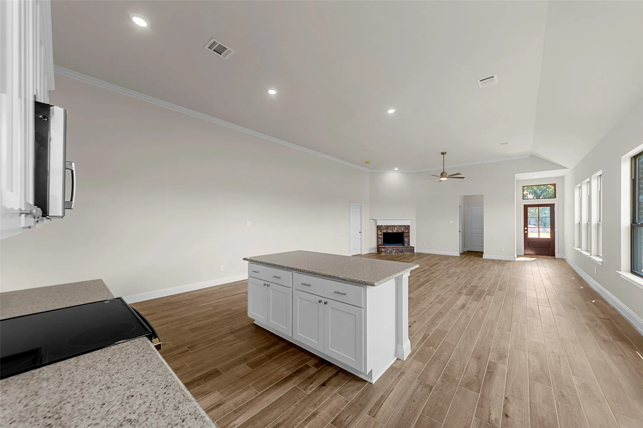 Open-concept living space with vaulted ceilings, recessed lighting, wood-finish flooring, stone fireplace, and a kitchen island with stone countertops