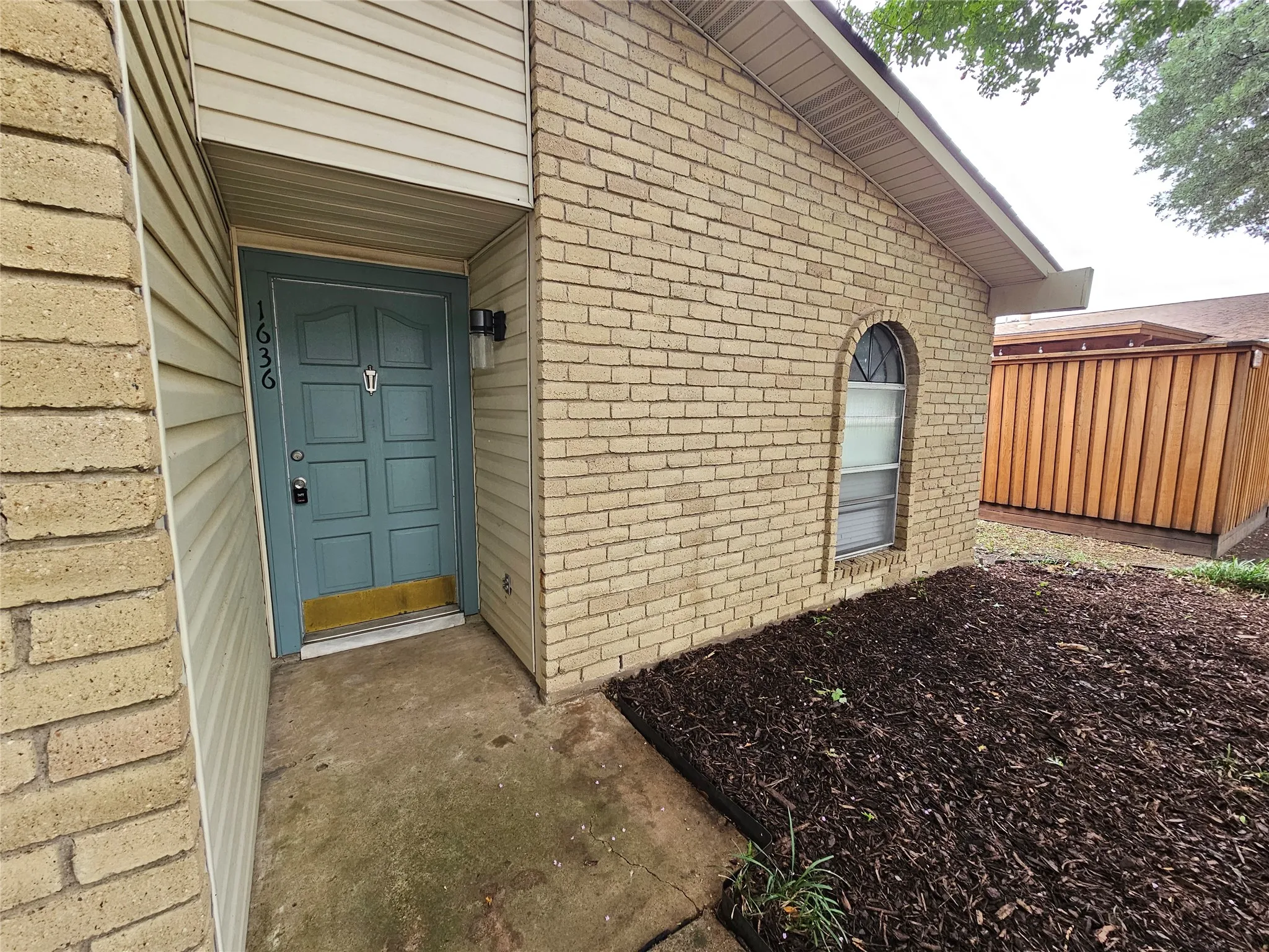 Brick exterior with siding accents, paneled entry door, arched window, and mulched landscaping