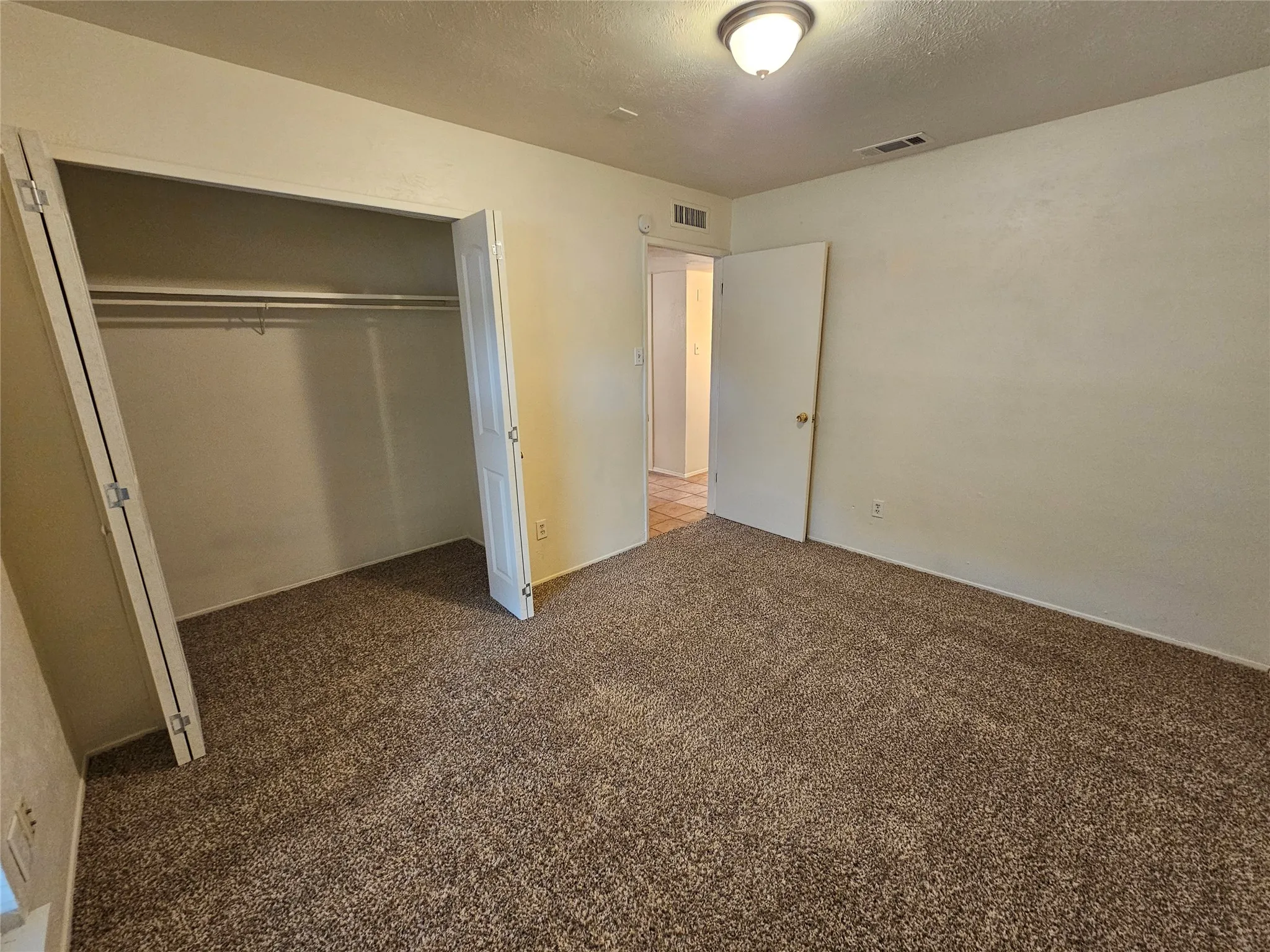Carpeted room featuring a built-in closet with bi-fold doors and overhead lighting
