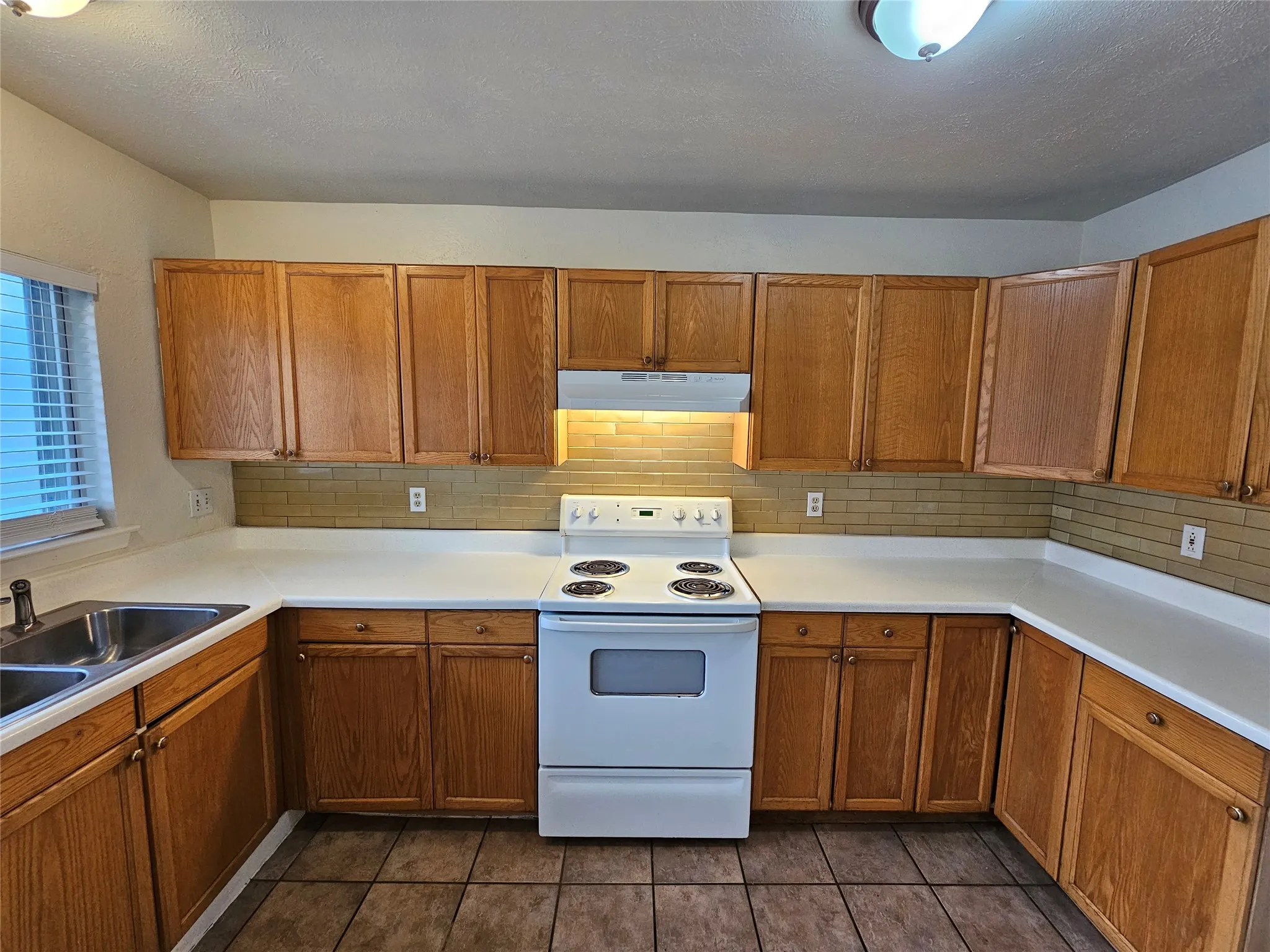 U-shaped kitchen with wood-finish cabinetry, white countertops, a double basin sink, and a white electric range