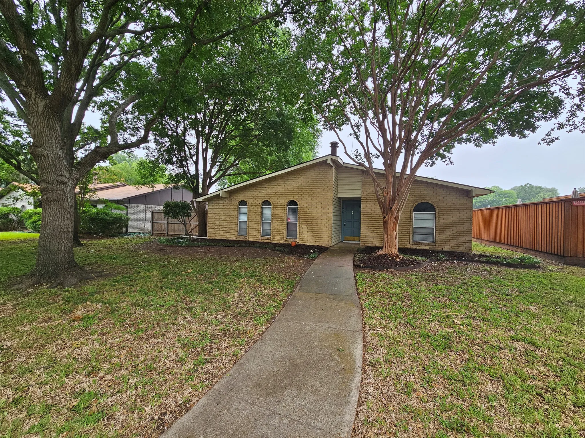 Brick facade home with arched windows, mature trees, and a wooden privacy fence