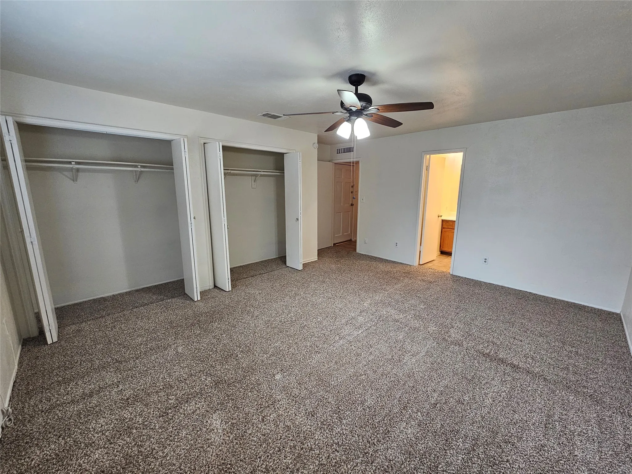 Neutral-toned carpeting, ample closet space with bi-fold doors, and a ceiling fan with integrated lighting