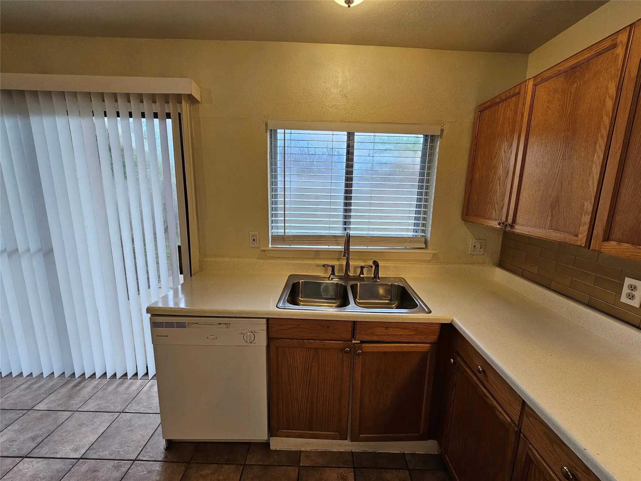 Kitchen featuring wood cabinetry, a double basin stainless steel sink, a dishwasher, and tiled flooring