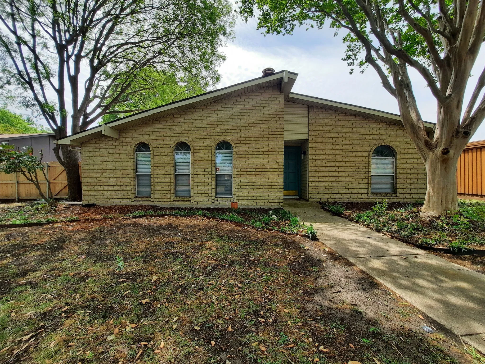 Brick exterior with arched windows, a front entry door, and mature trees