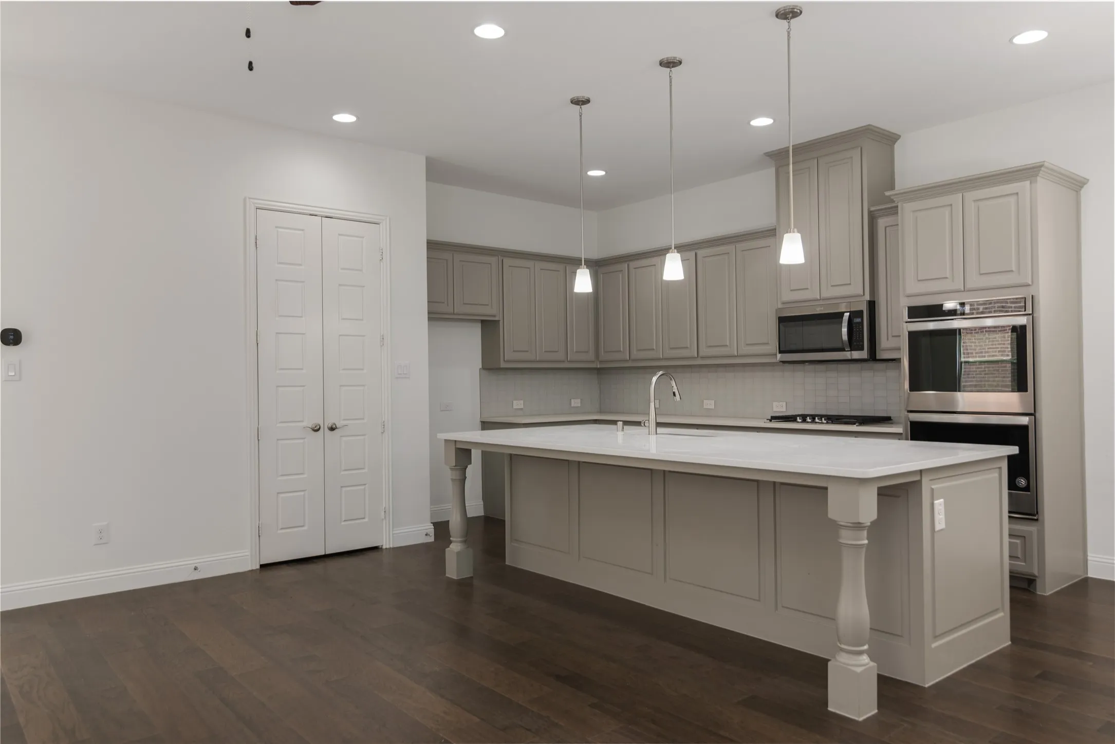 Kitchen with an expansive island featuring a large sink and pendant lighting, stainless steel double ovens, a built-in microwave, extensive cabinetry, and wood-finish flooring