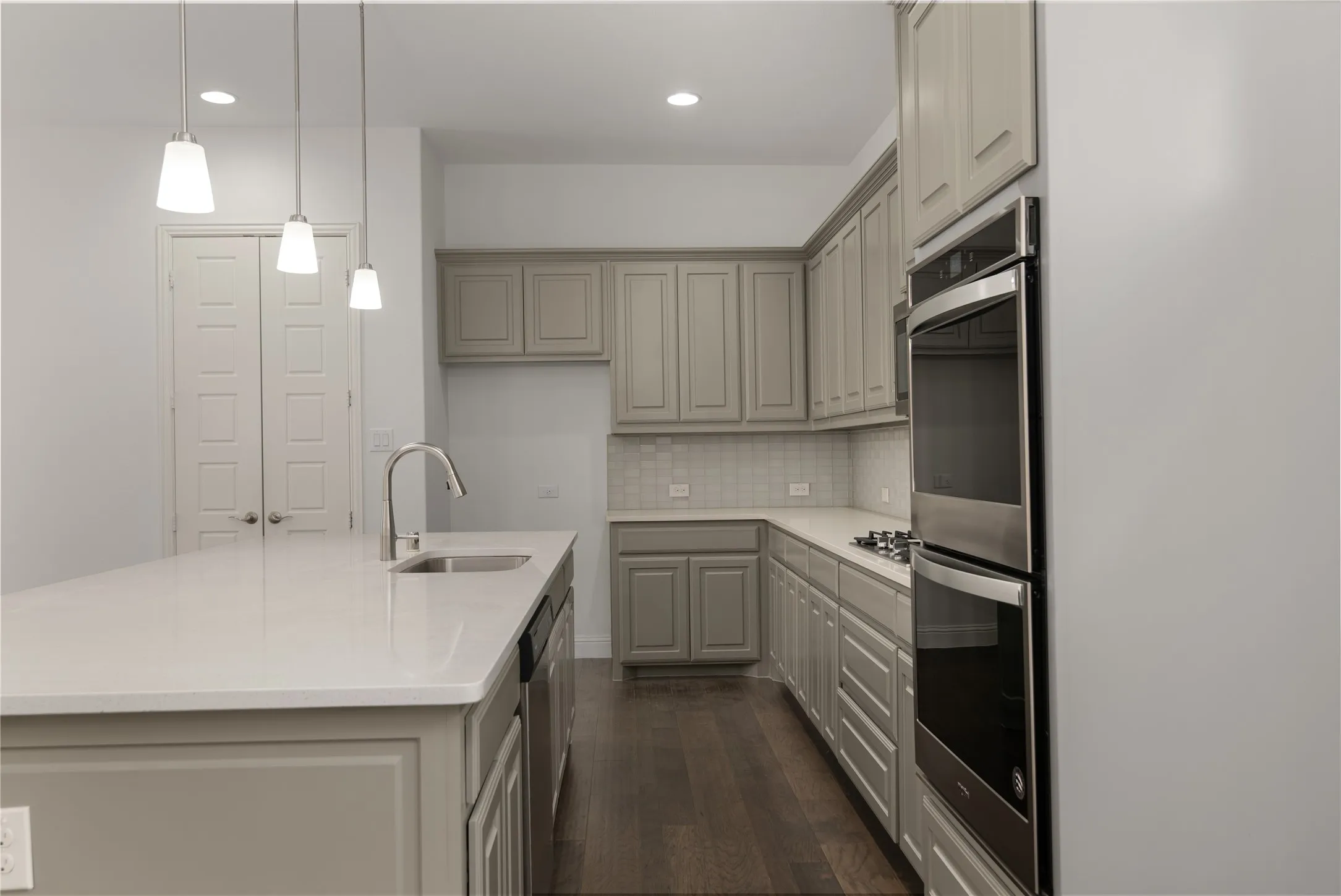 Kitchen featuring an island with undermount sink, pendant lighting, stainless steel double ovens, a gas cooktop, and wood-finish flooring