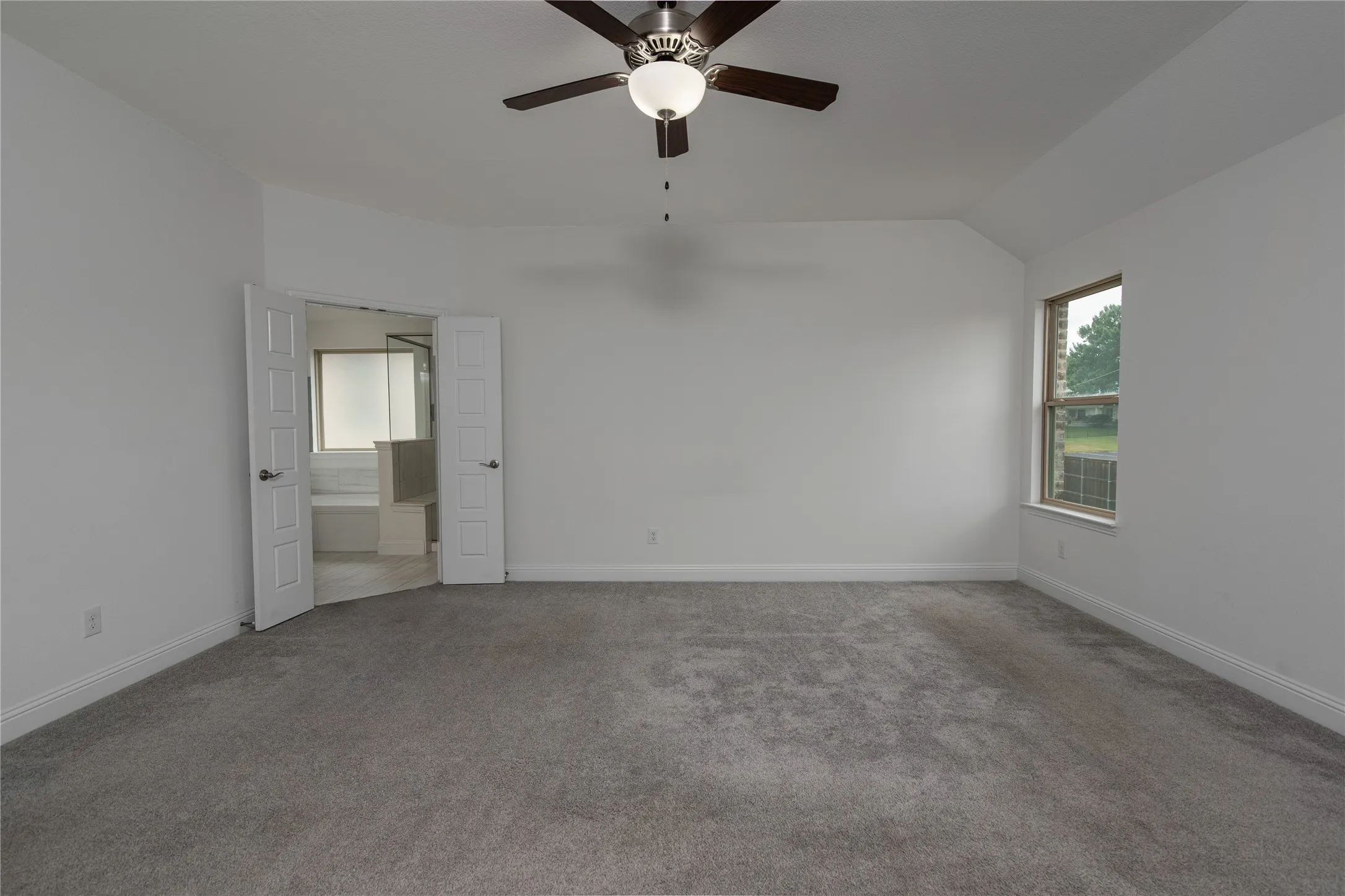 Spacious bedroom featuring neutral walls, plush carpeting, ceiling fan with integrated lighting, and abundant natural light from a side window