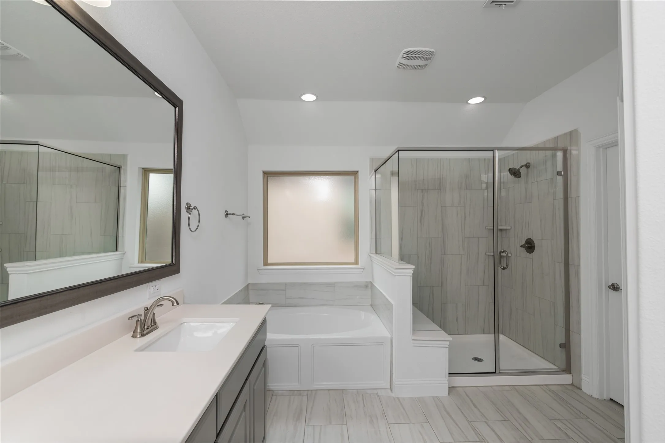 Bathroom featuring a built-in soaking tub, a separate glass-enclosed shower with tile surround, a single vanity with an integrated sink and light-toned countertop, and recessed lighting