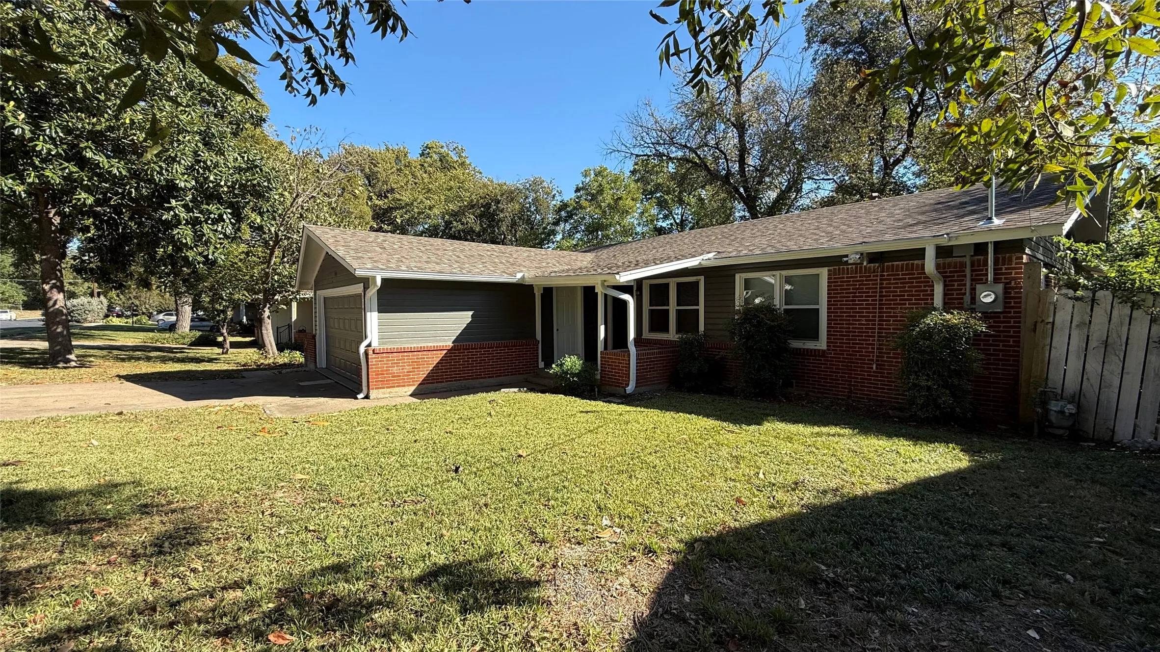 Ranch-style exterior featuring a combination of brick and siding, an attached garage, a front yard with mature trees, and a concrete driveway