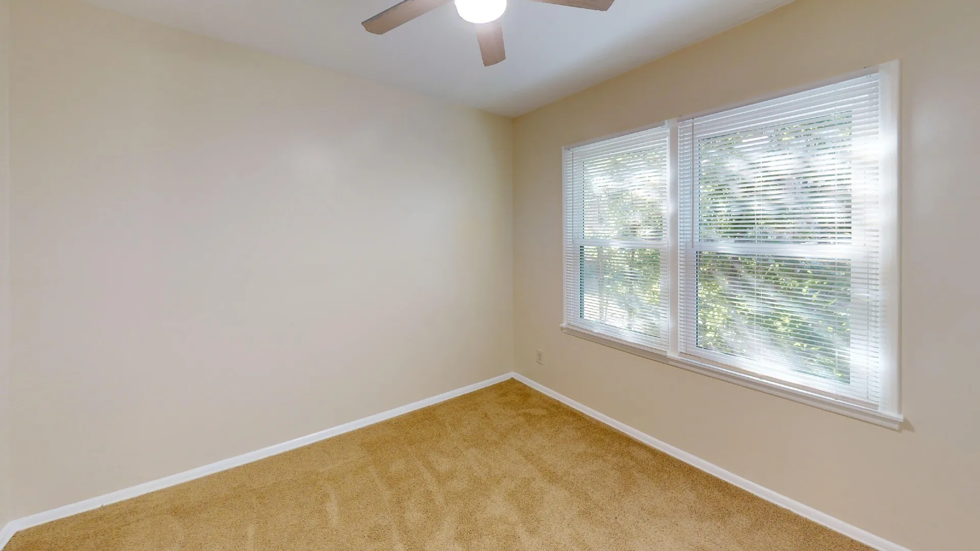 Neutral tone wall paint, carpet flooring, two pane windows with horizontal blinds, and a ceiling fan with integrated lighting