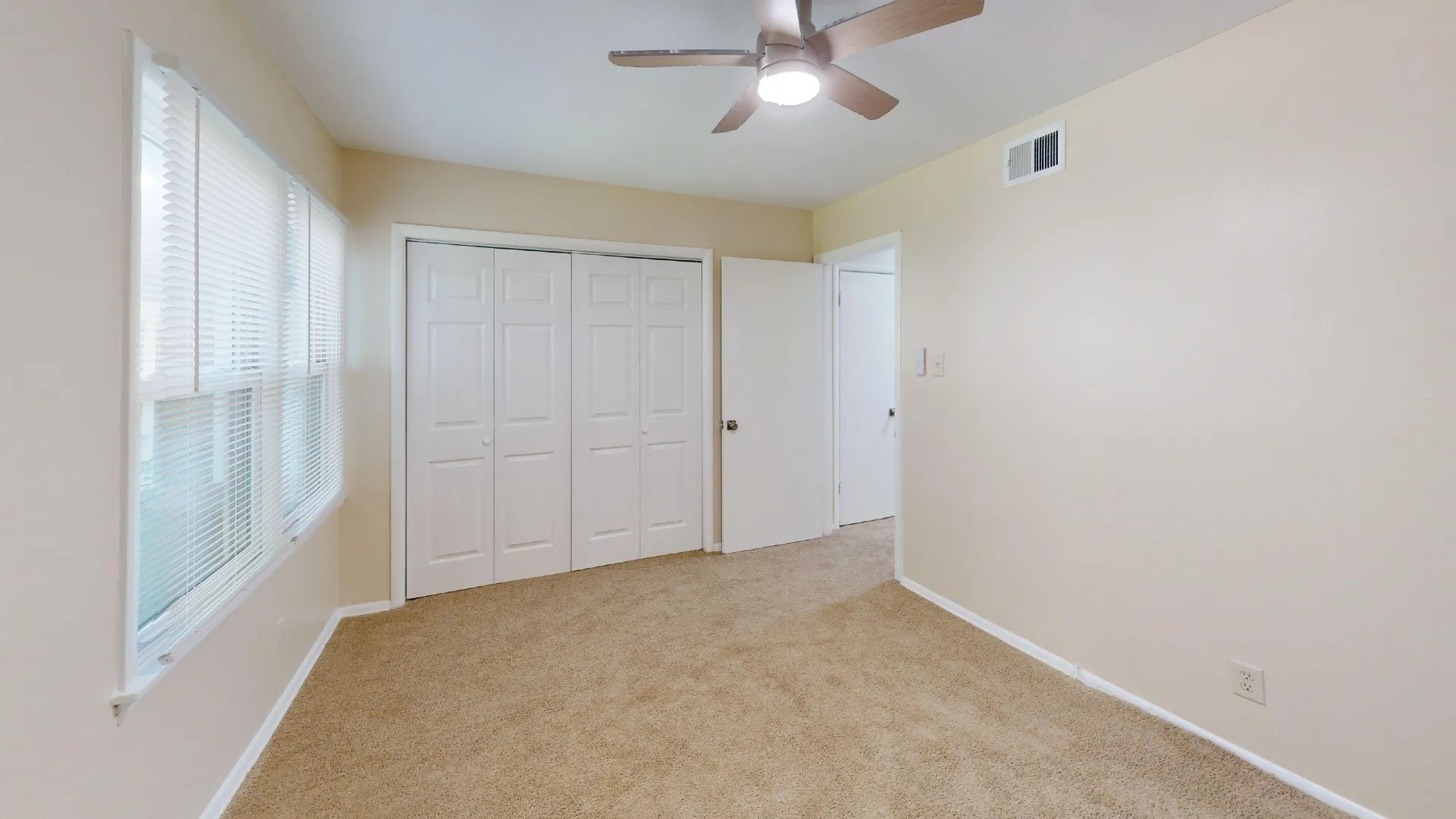 Plush carpeting, ceiling fan with integrated lighting, window with blinds, and white bi-fold closet doors