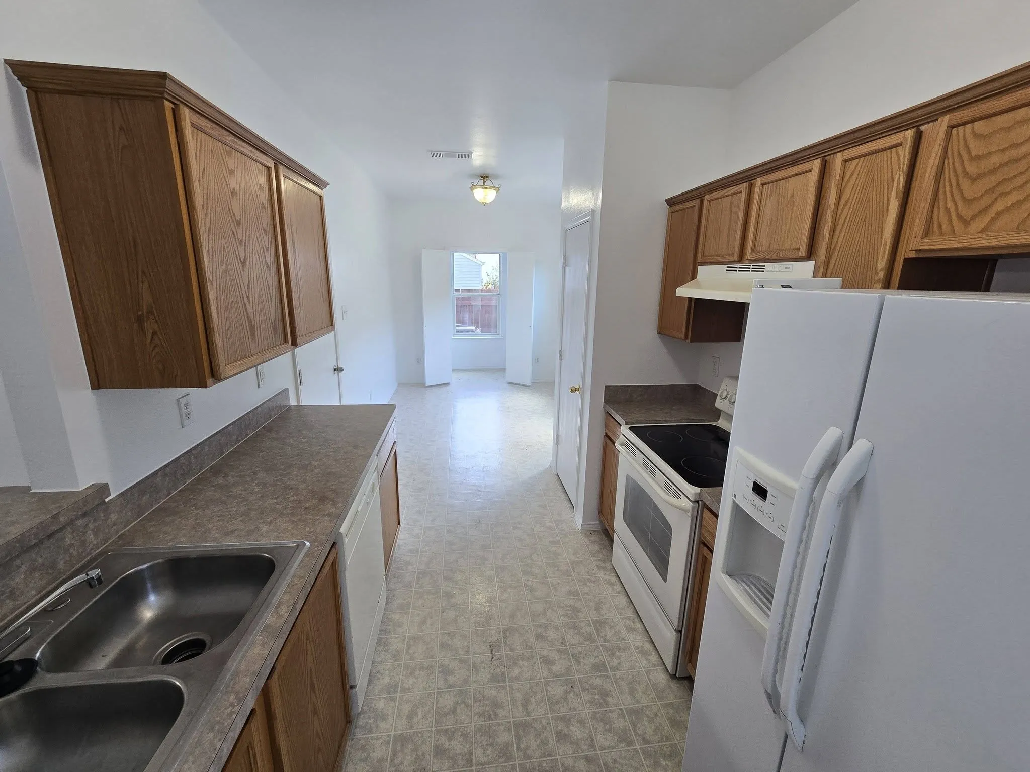 Kitchen featuring wood cabinetry, laminate countertops, a double basin stainless steel sink, and durable vinyl flooring
