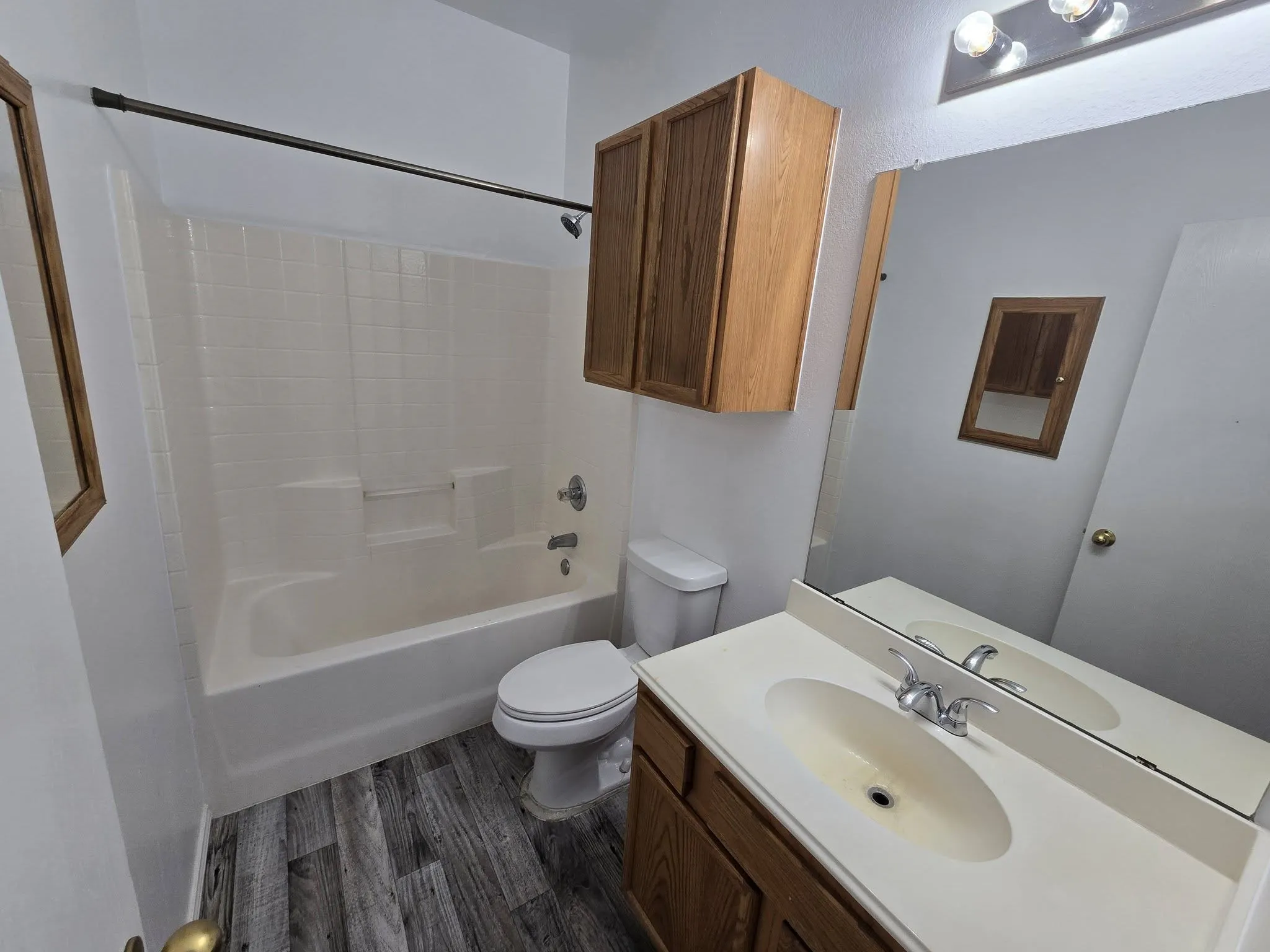 Wood-finish vinyl flooring, full bathtub with shower, wood vanity with integrated sink, wood-finish wall cabinet, and vanity​​‌​​​​‌​​‌‌​‌‌​​​‌‌​‌​‌​‌​​​‌​​ mirror
