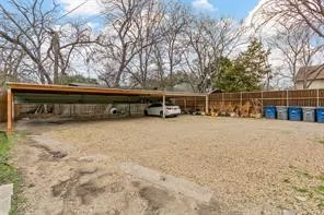 Expansive gravel parking area with attached carport for covered parking, complemented by a wood-paneled privacy fence