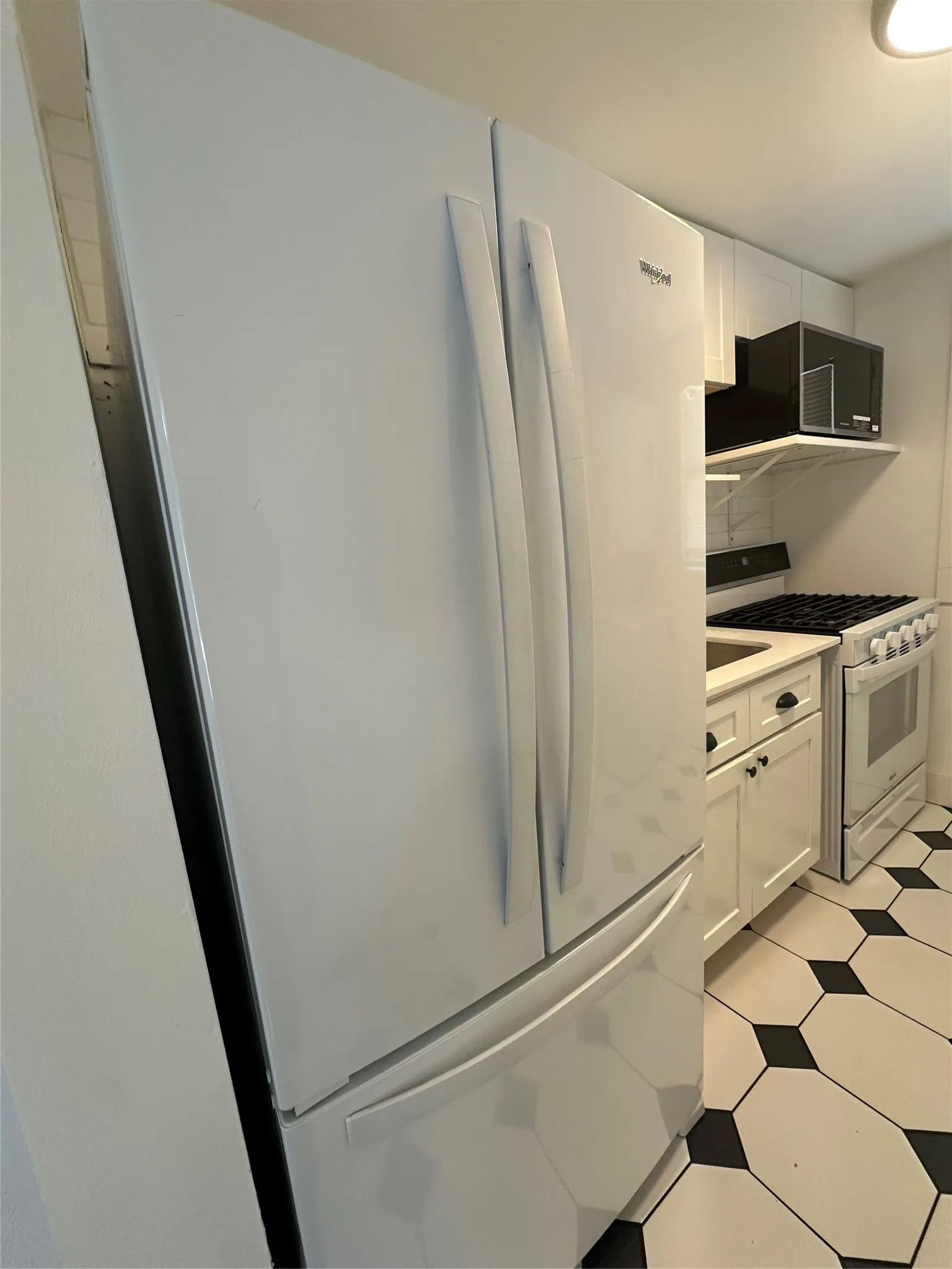 Spacious kitchen featuring a white French-door refrigerator, dual electric ranges with black backsplash, upper cabinetry with integrated microwave, and black-and-white diamond-pattern tile flooring
