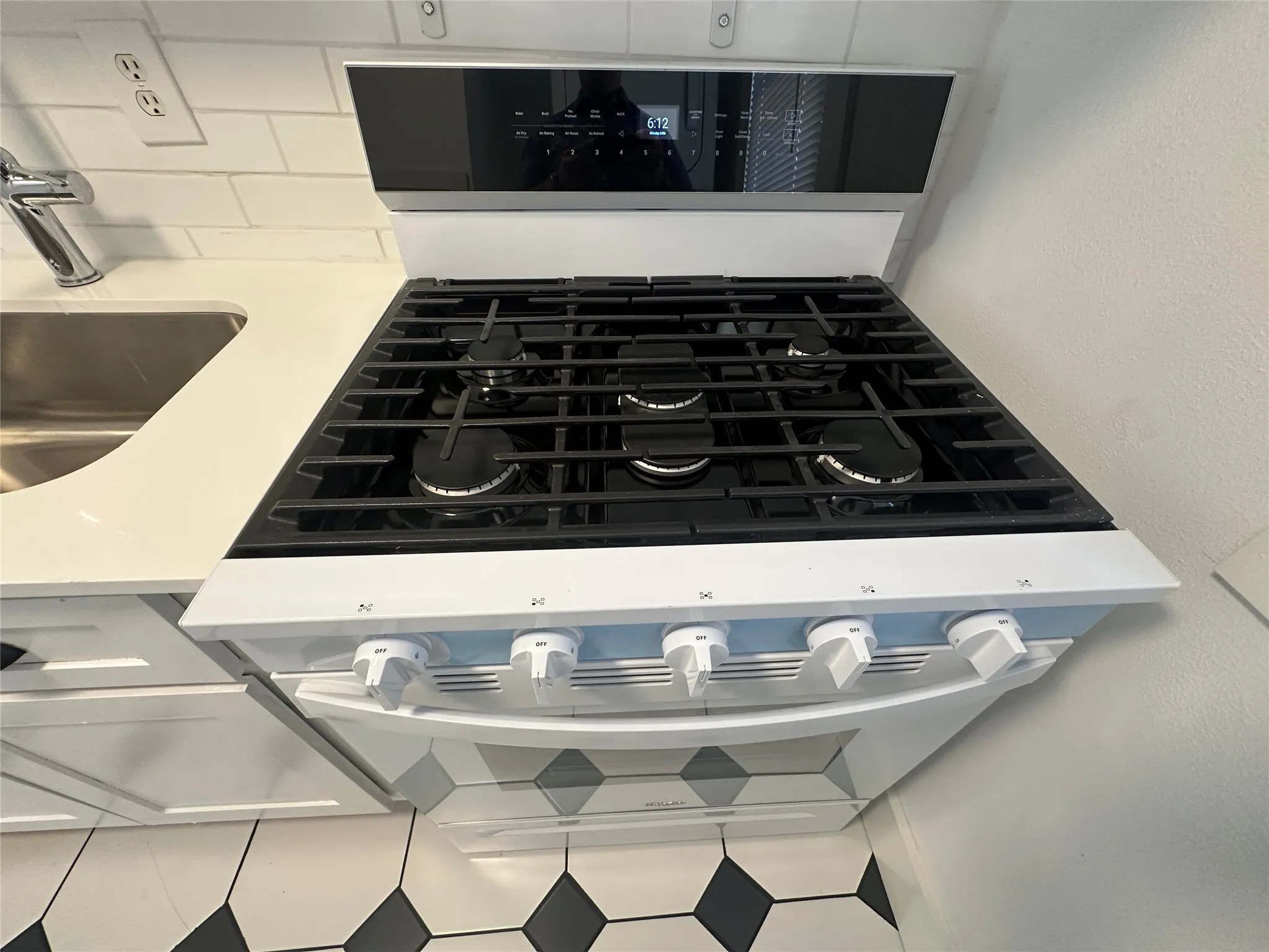 Gas range with a digital control panel, solid surface countertops, subway tile backsplash, stainless steel sink, and patterned floor tiles